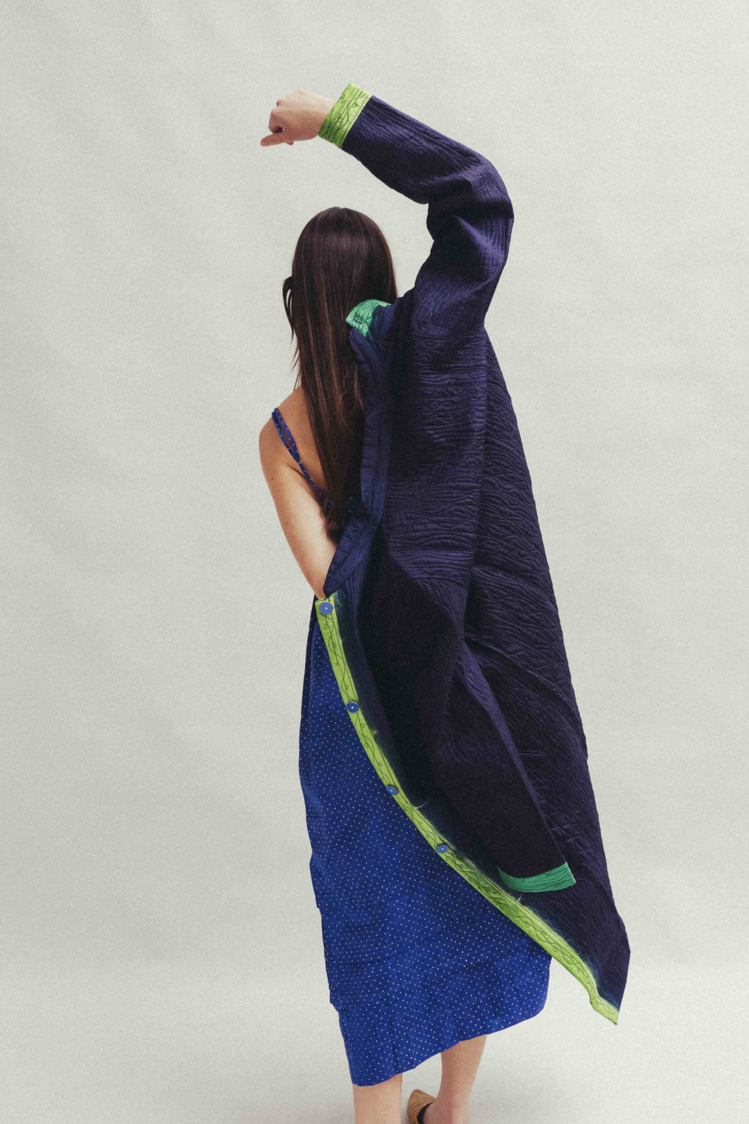 Model is wearing the Folklore 18 handmade silk coat by Injiri, featuring a navy blue exterior, green lining, 100% silk, and luxurious artisan craftsmanship.
