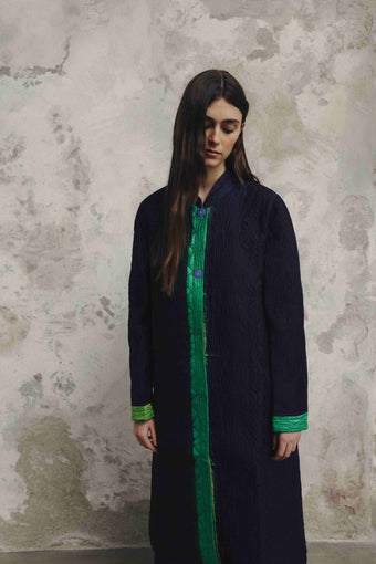 Model is wearing the Folklore 18 handmade silk coat by Injiri, featuring a navy blue exterior, green lining, 100% silk, and luxurious artisan craftsmanship.