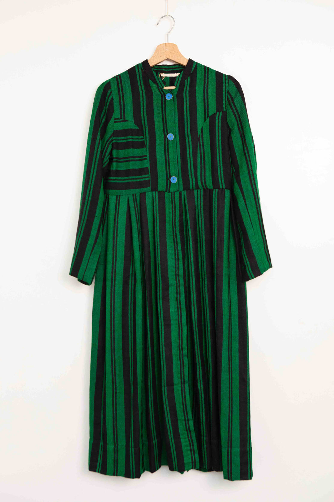 Model is wearing the Folklore 34 silk and wool striped dress by Injiri, featuring bold green and black stripes and sky blue buttons, artisan-made in India.