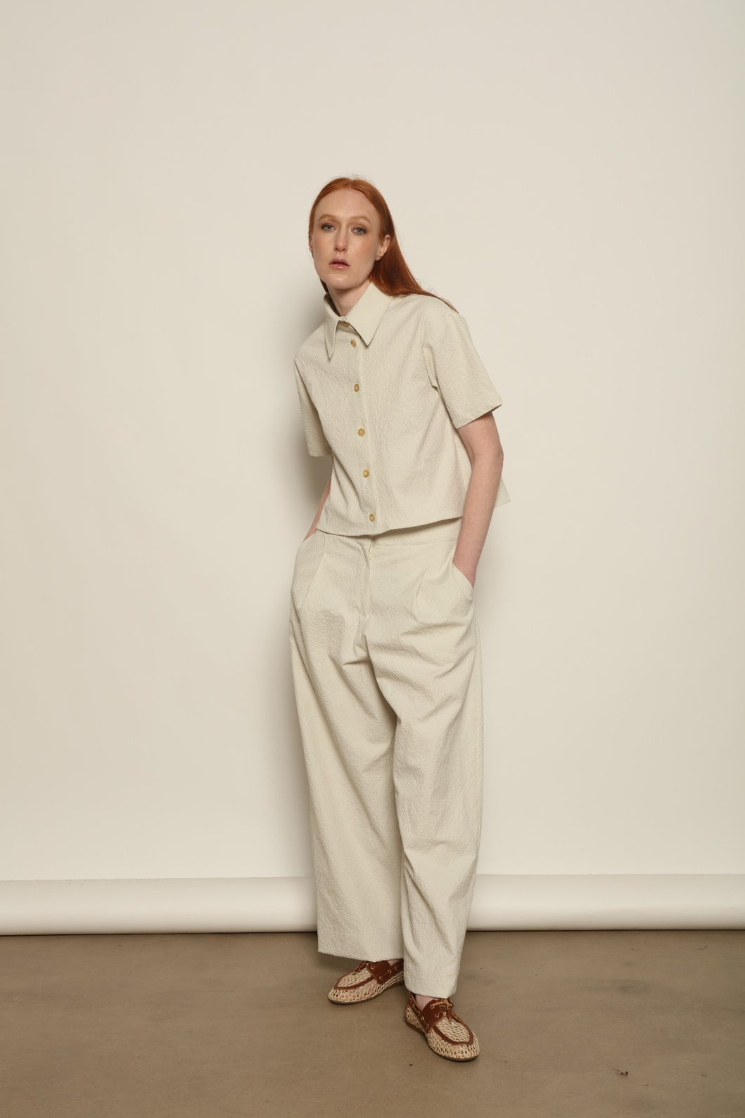 Model is wearing the Gabriella seersucker trousers from the House of Nomad Stories selection, lightweight and breathable women’s summer pants made in Italy, featuring a relaxed tailored silhouette designed for effortless movement and warm weather.