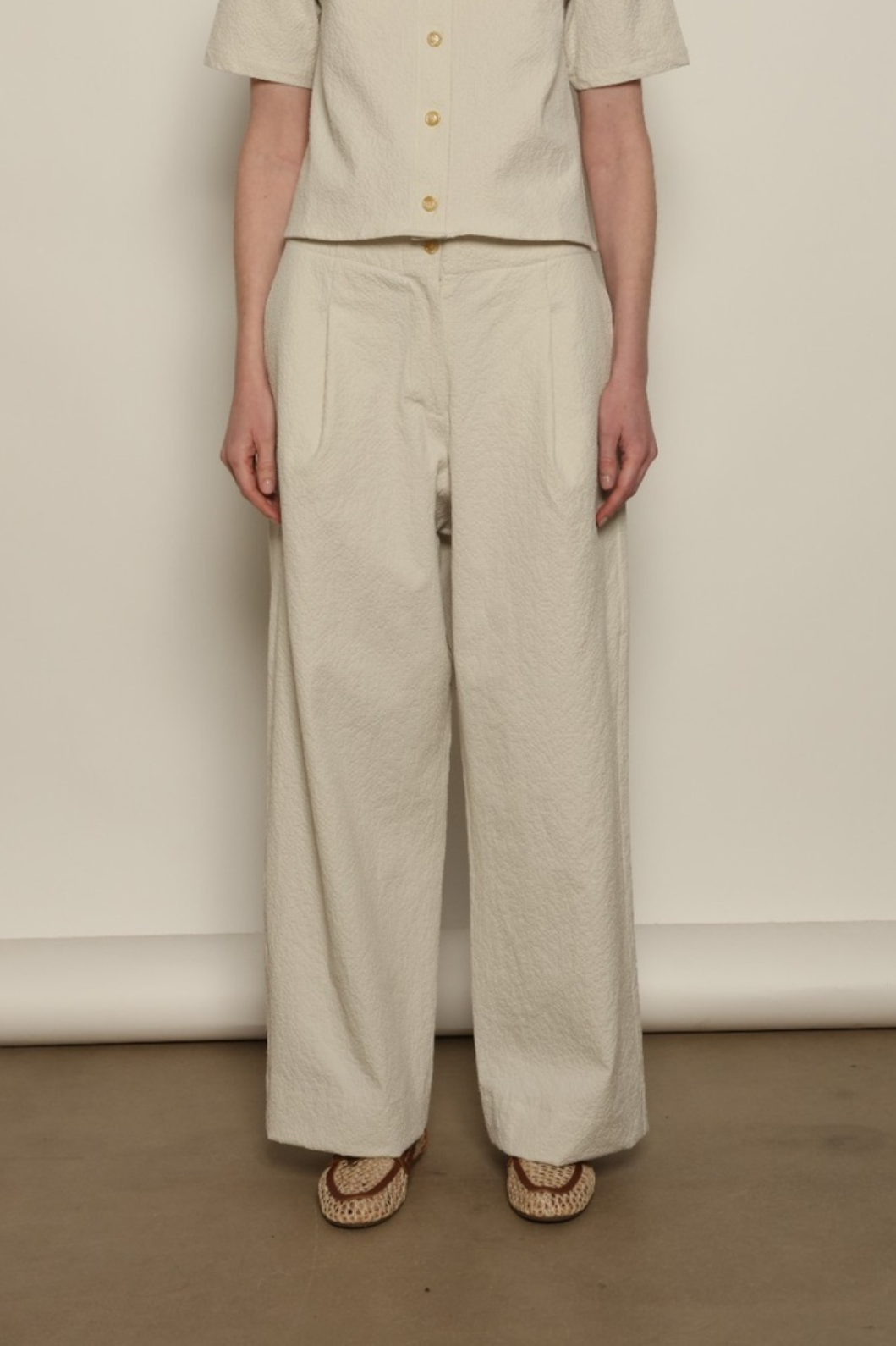 Model is wearing the Gabriella seersucker trousers from the House of Nomad Stories selection, lightweight and breathable women’s summer pants made in Italy, featuring a relaxed tailored silhouette designed for effortless movement and warm weather.