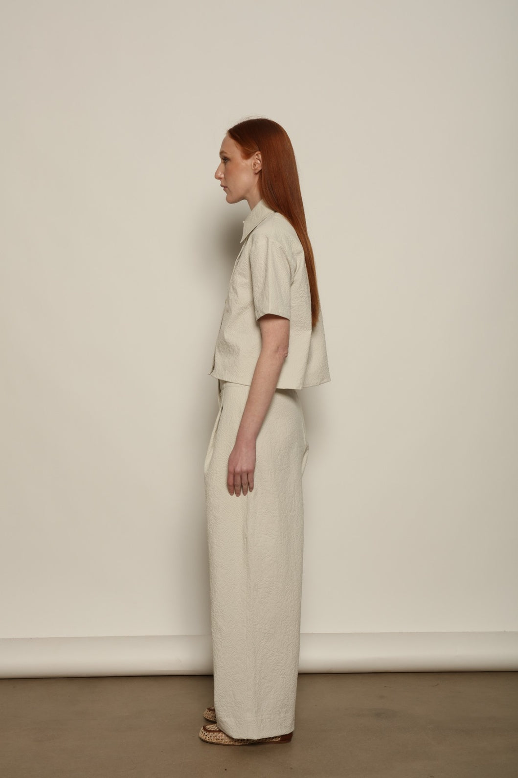 Model is wearing the Gabriella seersucker trousers from the House of Nomad Stories selection, lightweight and breathable women’s summer pants made in Italy, featuring a relaxed tailored silhouette designed for effortless movement and warm weather.