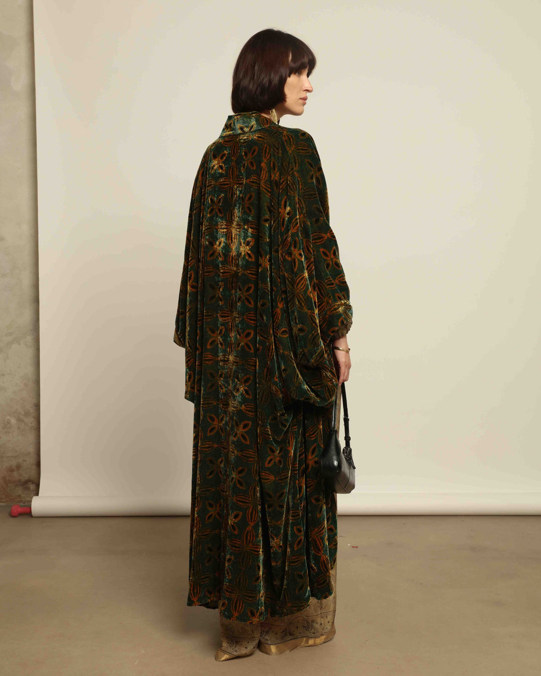 Model is wearing a golden sage silk and velvet abaya with geometric patterns, featuring a flowing elegant silhouette, perfect for modern and regal styling.