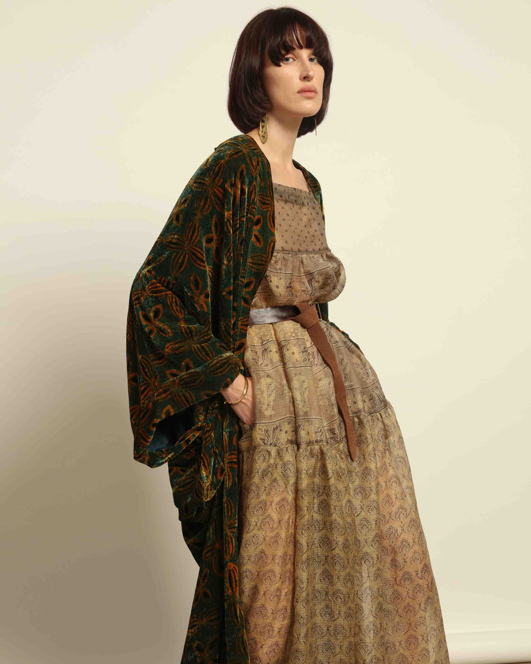 Model is wearing a golden sage silk and velvet abaya with geometric patterns, featuring a flowing elegant silhouette, perfect for modern and regal styling.