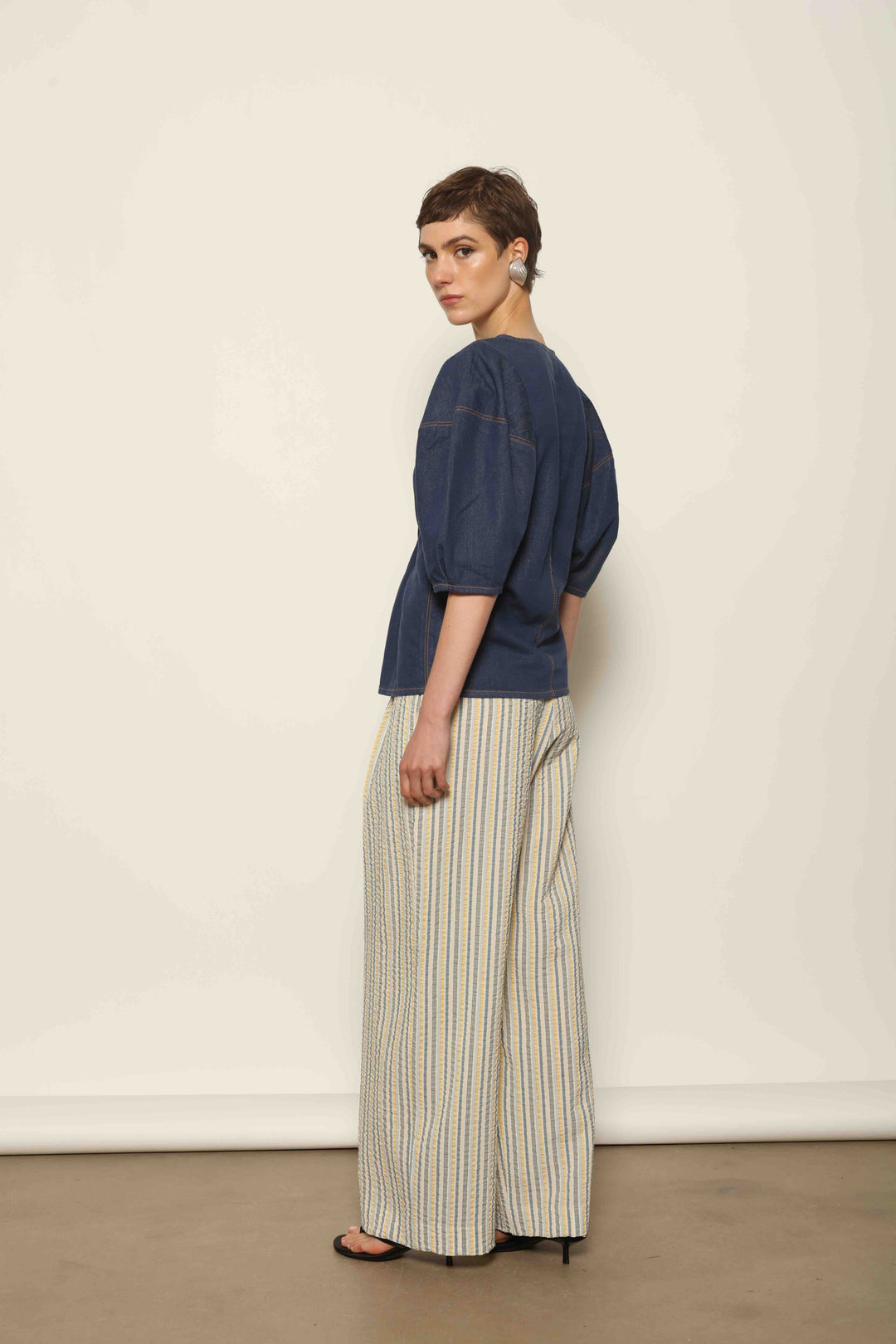 Model wearing the Blouse Bubble Brut in cotton denim by Happy Haus, featuring balloon sleeves, straight-cut silhouette, round neckline, and tobacco topstitching in a lightweight, breathable fabric.