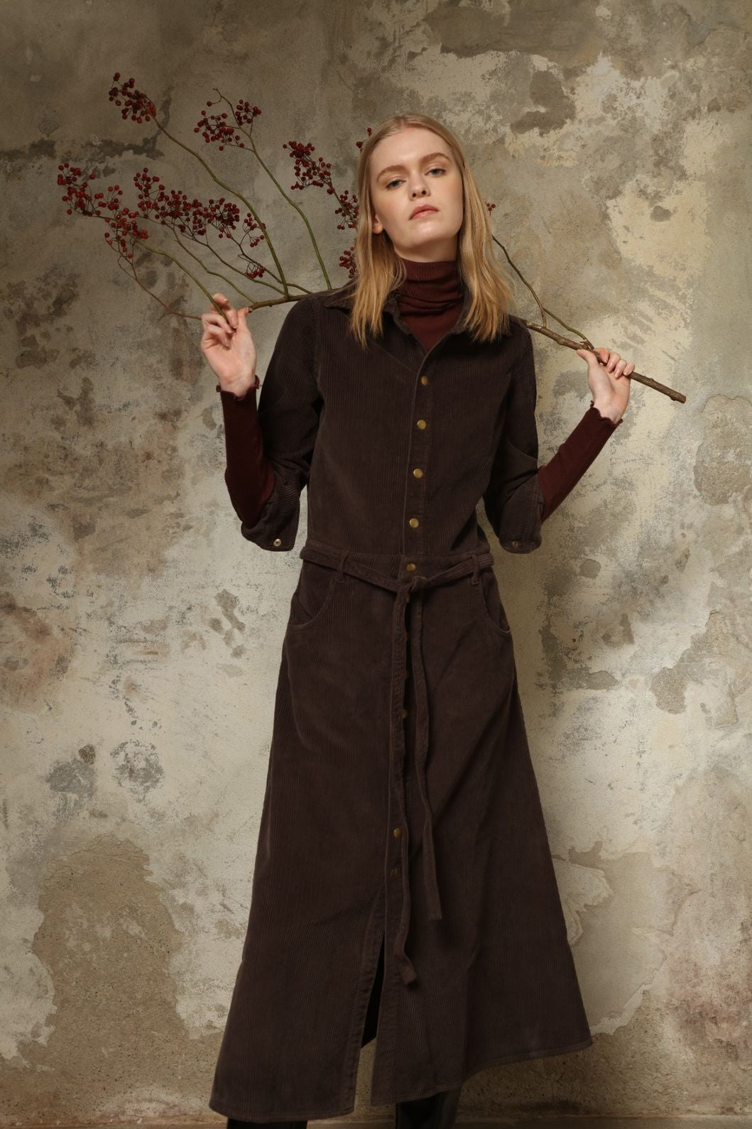Model is wearing La Robe Trompe L’Oeil in Chocolate by Happy Haus, a corduroy cotton trompe-l’œil dress with removable belt, tulip-shaped pockets and brass snaps, curated in the House of Nomad Stories selection.