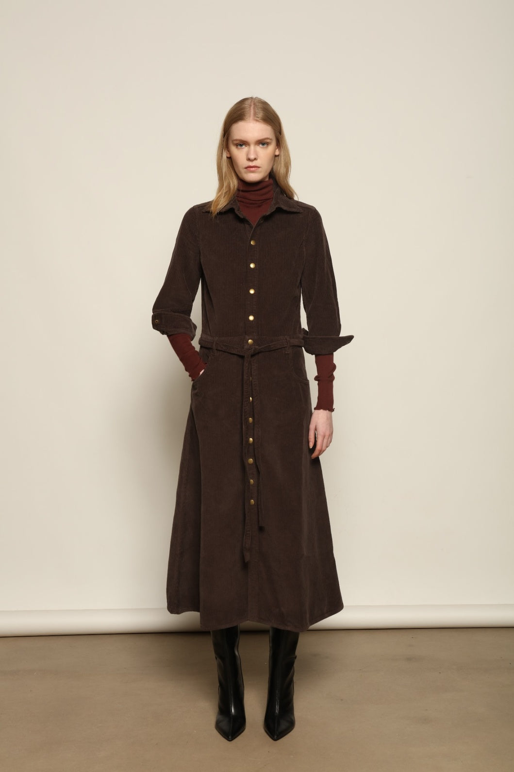 Model is wearing La Robe Trompe L’Oeil in Chocolate by Happy Haus, a corduroy cotton trompe-l’œil dress with removable belt, tulip-shaped pockets and brass snaps, curated in the House of Nomad Stories selection.