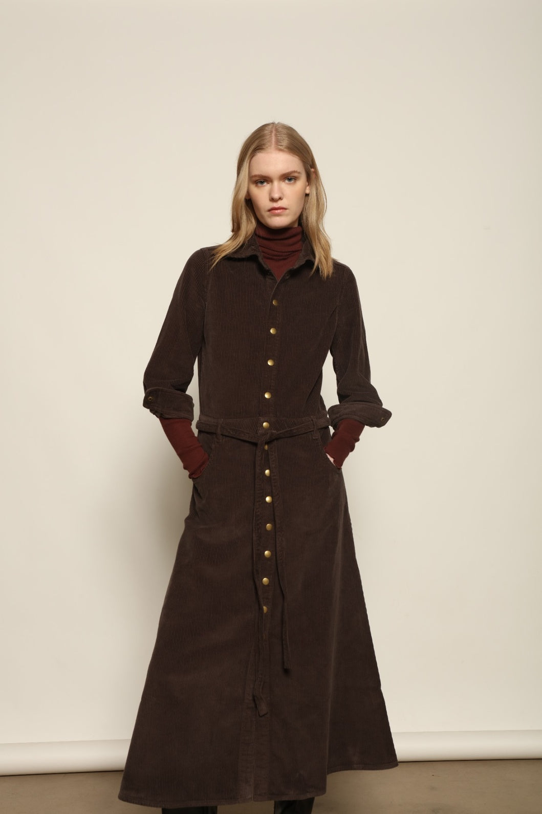 Model is wearing La Robe Trompe L’Oeil in Chocolate by Happy Haus, a corduroy cotton trompe-l’œil dress with removable belt, tulip-shaped pockets and brass snaps, curated in the House of Nomad Stories selection.
