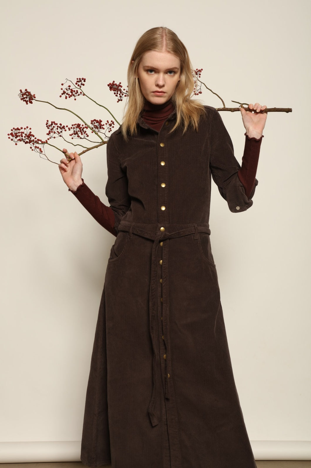 Model is wearing La Robe Trompe L’Oeil in Chocolate by Happy Haus, a corduroy cotton trompe-l’œil dress with removable belt, tulip-shaped pockets and brass snaps, curated in the House of Nomad Stories selection.