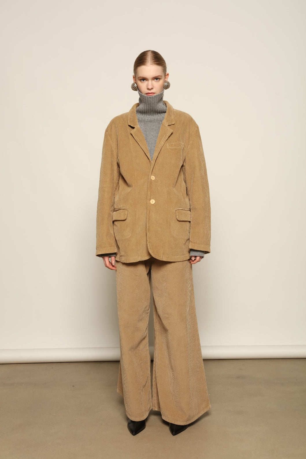 Model is wearing Le Pantalon Over Chino in Beige by Happy Haus, flared oversized corduroy cotton trousers with removable belt, corozo buttons and peacock embroidery, curated in the House of NNomad Stories selection.