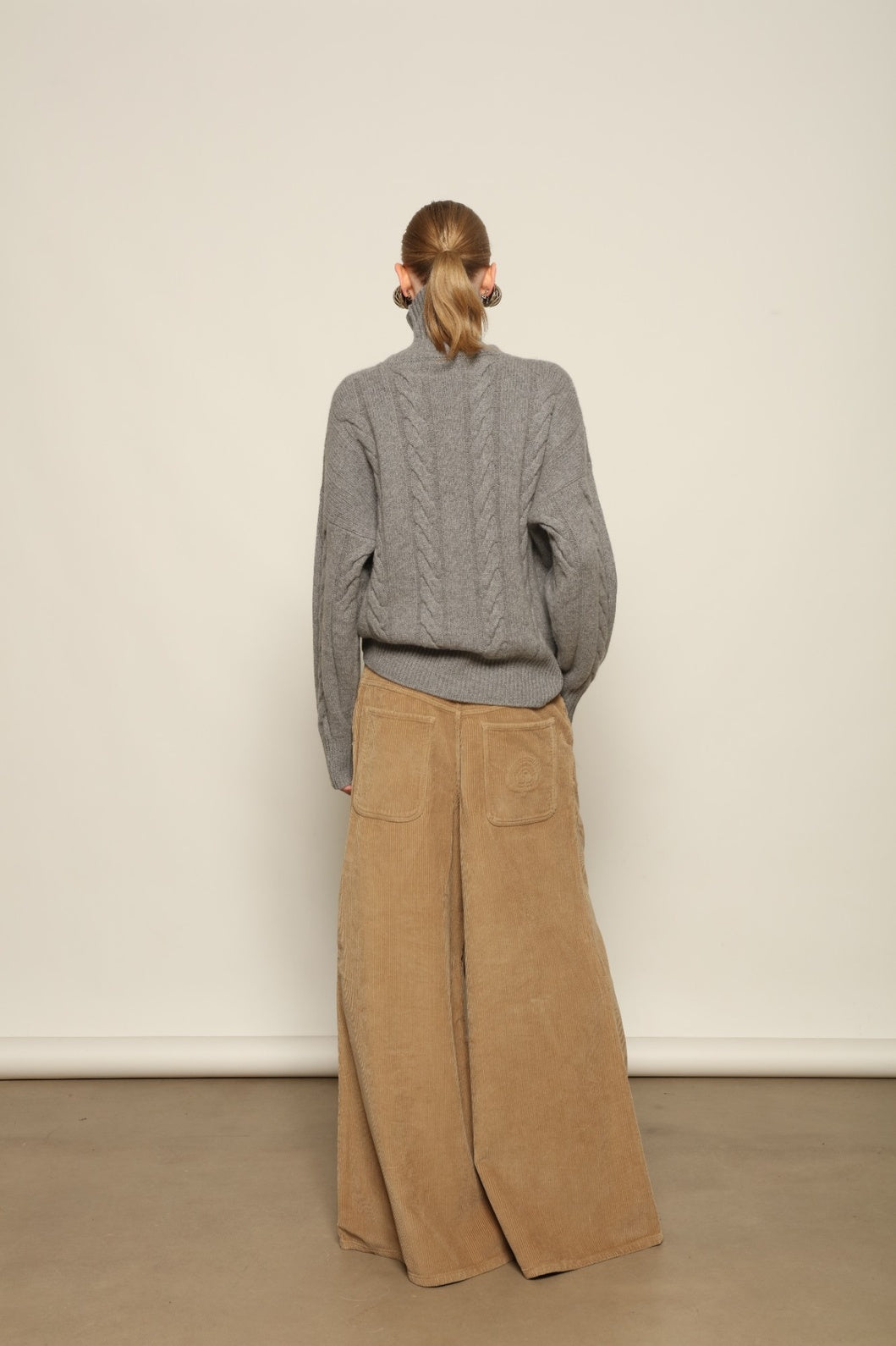 Model is wearing Le Pantalon Over Chino in Beige by Happy Haus, flared oversized corduroy cotton trousers with removable belt, corozo buttons and peacock embroidery, curated in the House of Nomad Stories selection.