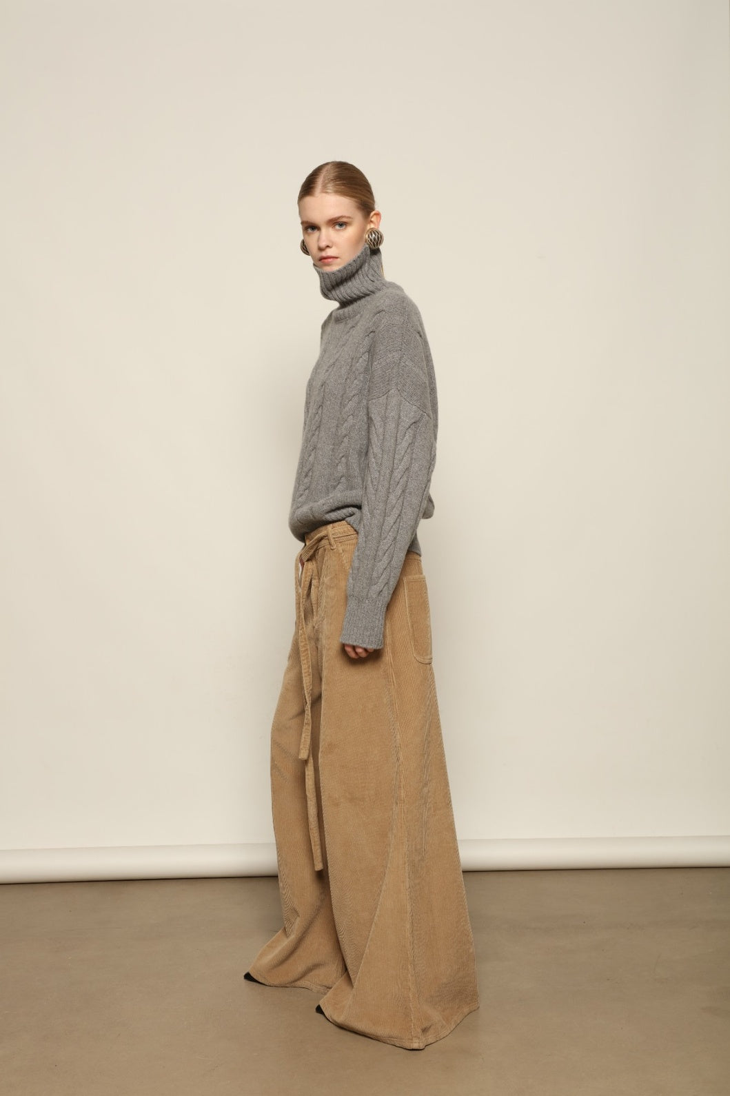 Model is wearing Le Pantalon Over Chino in Beige by Happy Haus, flared oversized corduroy cotton trousers with removable belt, corozo buttons and peacock embroidery, curated in the House of Nomad Stories selection.