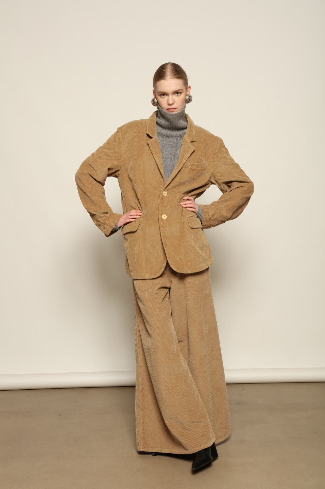 Model is wearing Le Pantalon Over Chino in Beige by Happy Haus, flared oversized corduroy cotton trousers with removable belt, corozo buttons and peacock embroidery, curated in the House of Nomad Stories selection.