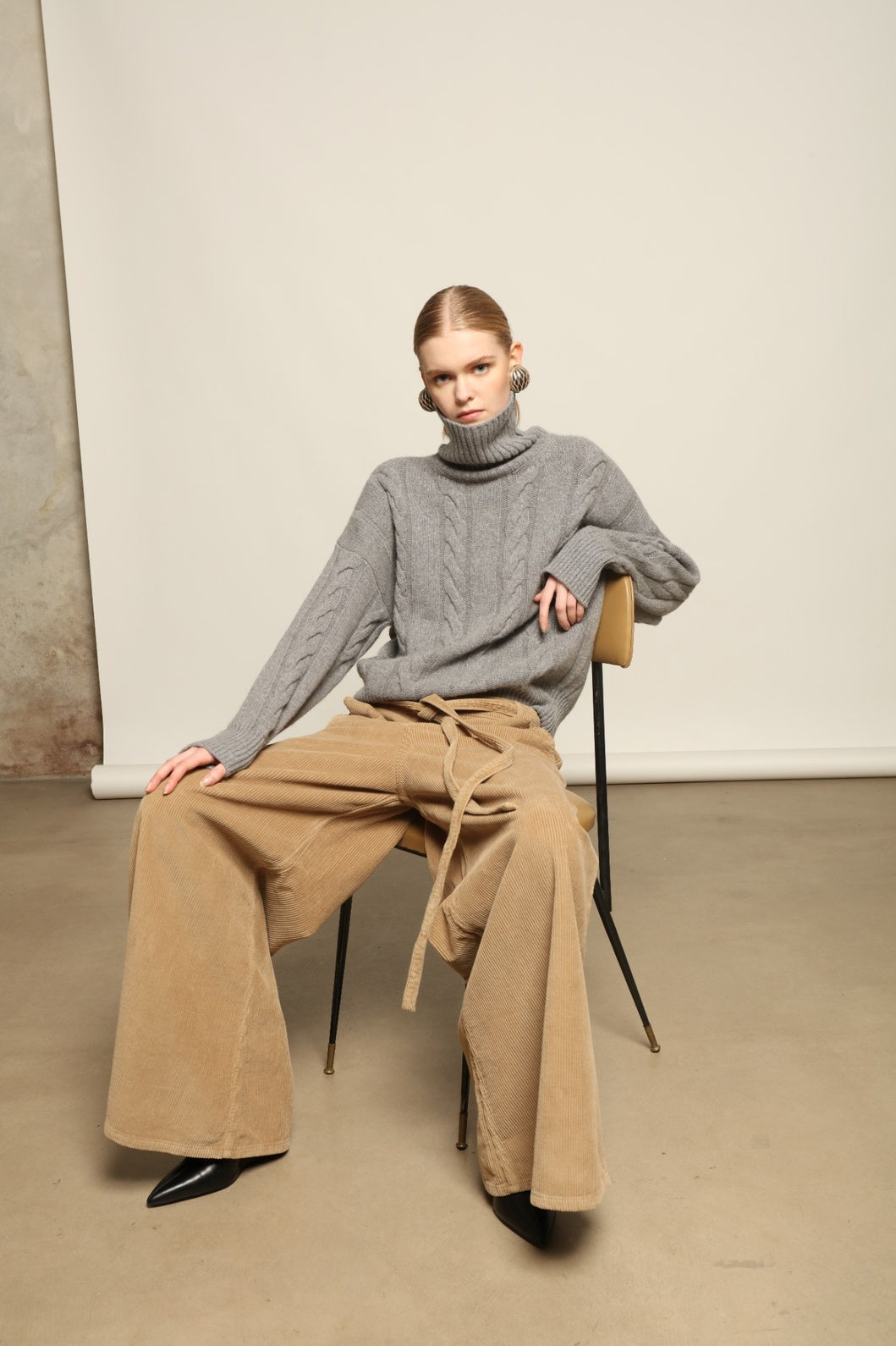 Model is wearing Le Pantalon Over Chino in Beige by Happy Haus, flared oversized corduroy cotton trousers with removable belt, corozo buttons and peacock embroidery, curated in the House of Nomad Stories selection.