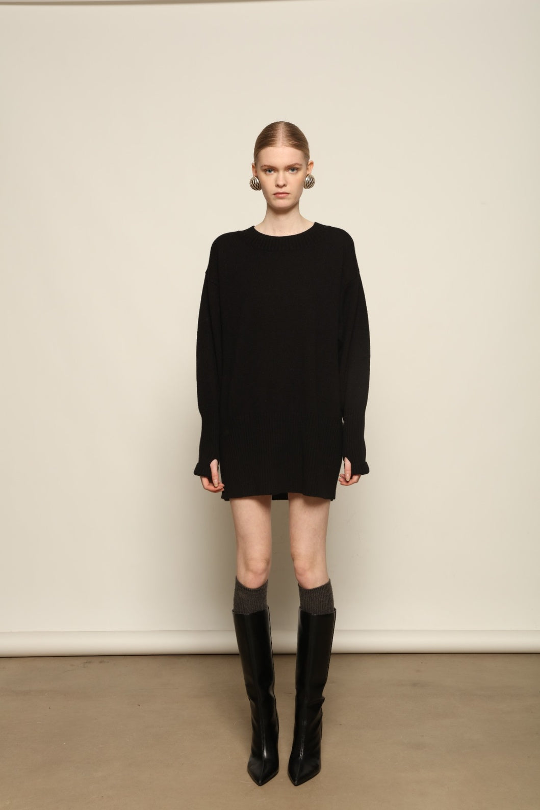 Model is wearing the Black Noemi Round Neck Long Sweater by House of Nomad Stories, a pure ethically sourced cashmere knit in deep black with long silhouette, round neckline and ribbed edges.