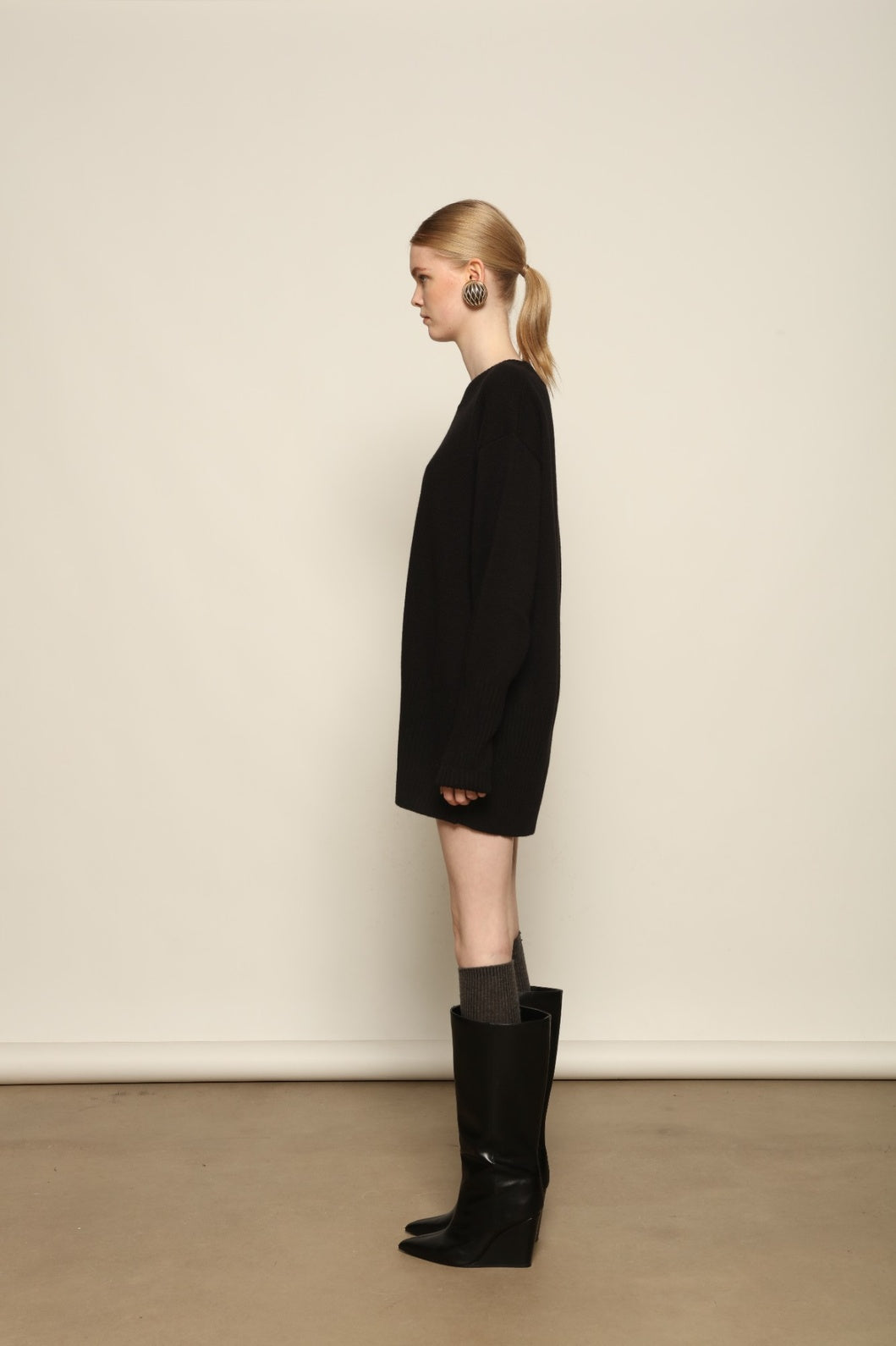 Model is wearing the Black Noemi Round Neck Long Sweater by House of Nomad Stories, a pure ethically sourced cashmere knit in deep black with long silhouette, round neckline and ribbed edges.