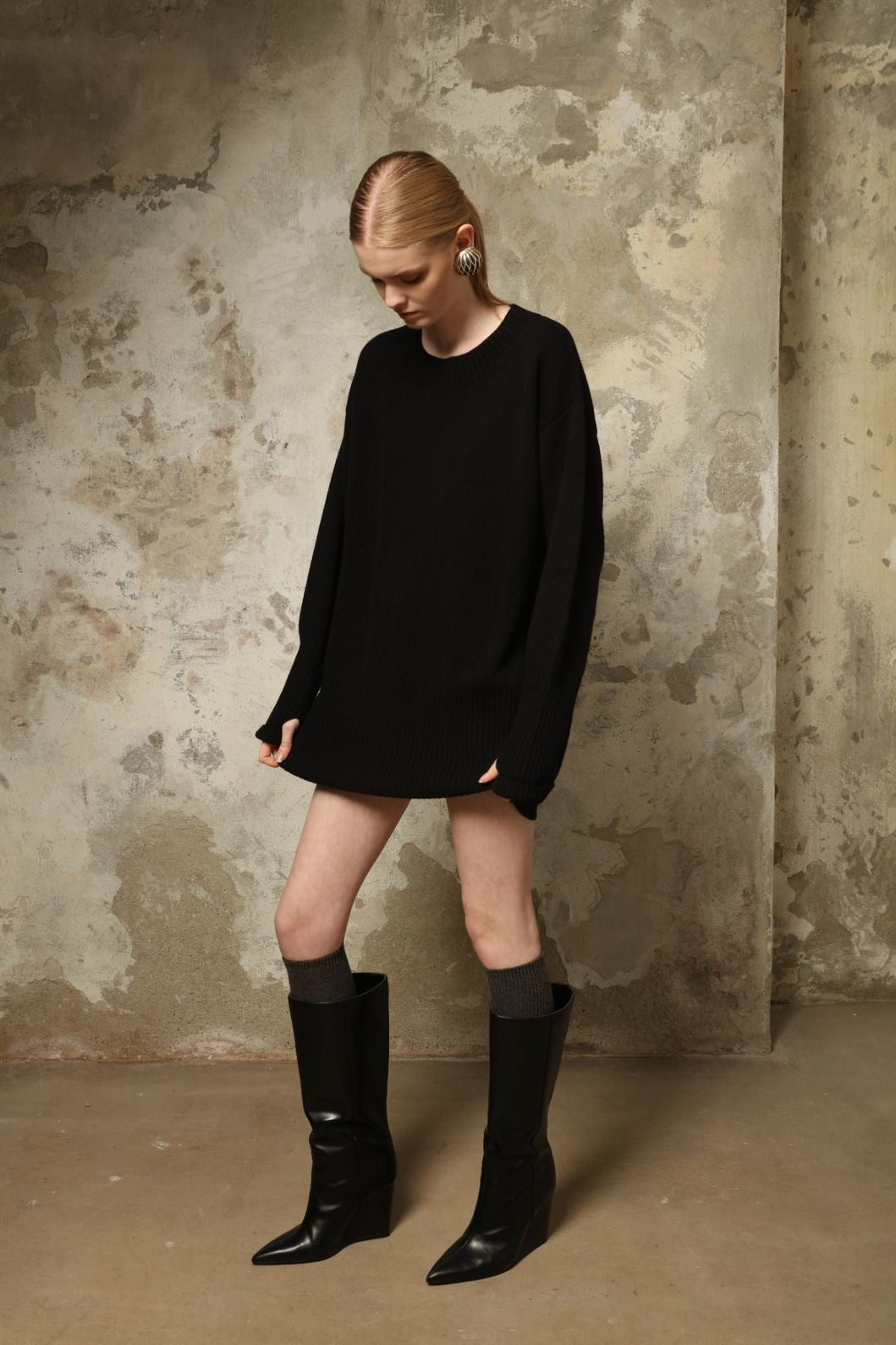 Model is wearing the Black Noemi Round Neck Long Sweater by House of Nomad Stories, a pure ethically sourced cashmere knit in deep black with long silhouette, round neckline and ribbed edges.