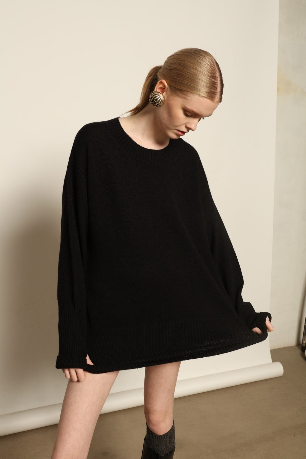 Model is wearing the Black Noemi Round Neck Long Sweater by House of Nomad Stories, a pure ethically sourced cashmere knit in deep black with long silhouette, round neckline and ribbed edges.
