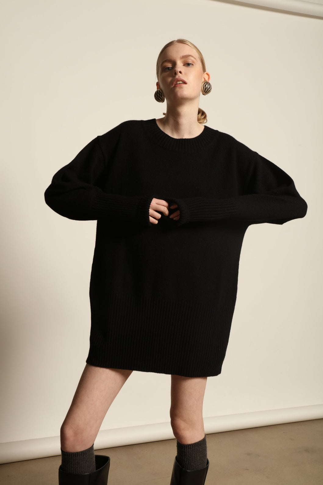 Model is wearing the Black Noemi Round Neck Long Sweater by House of Nomad Stories, a pure ethically sourced cashmere knit in deep black with long silhouette, round neckline and ribbed edges.