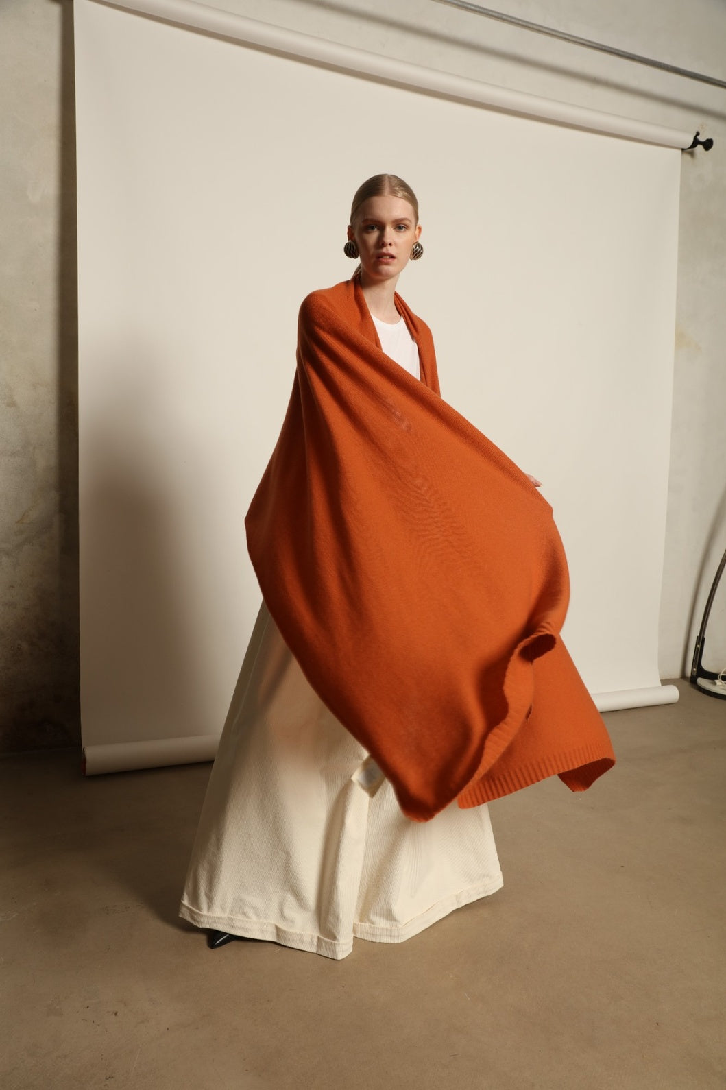 Model is wearing the Brick Leni Scarf by House of Nomad Stories, a pure ethically sourced cashmere scarf with refined texture, enduring softness and fluid drape in a warm brick tone.