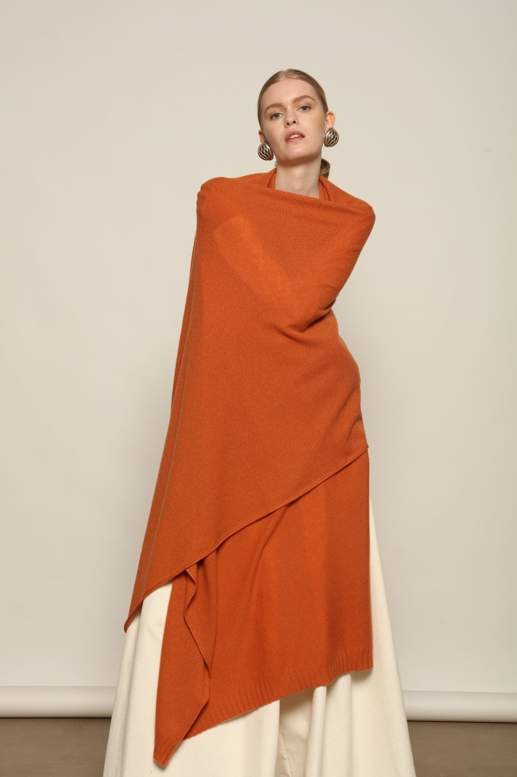 Model is wearing the Brick Leni Scarf by House of Nomad Stories, a pure ethically sourced cashmere scarf with refined texture, enduring softness and fluid drape in a warm brick tone.