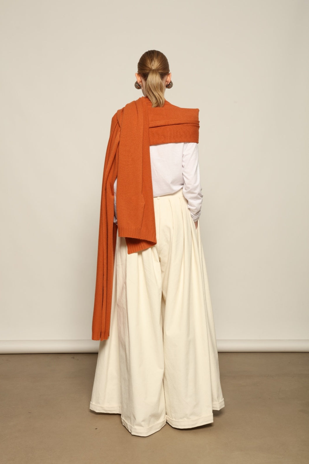Model is wearing the Brick Leni Scarf by House of Nomad Stories, a pure ethically sourced cashmere scarf with refined texture, enduring softness and fluid drape in a warm brick tone.