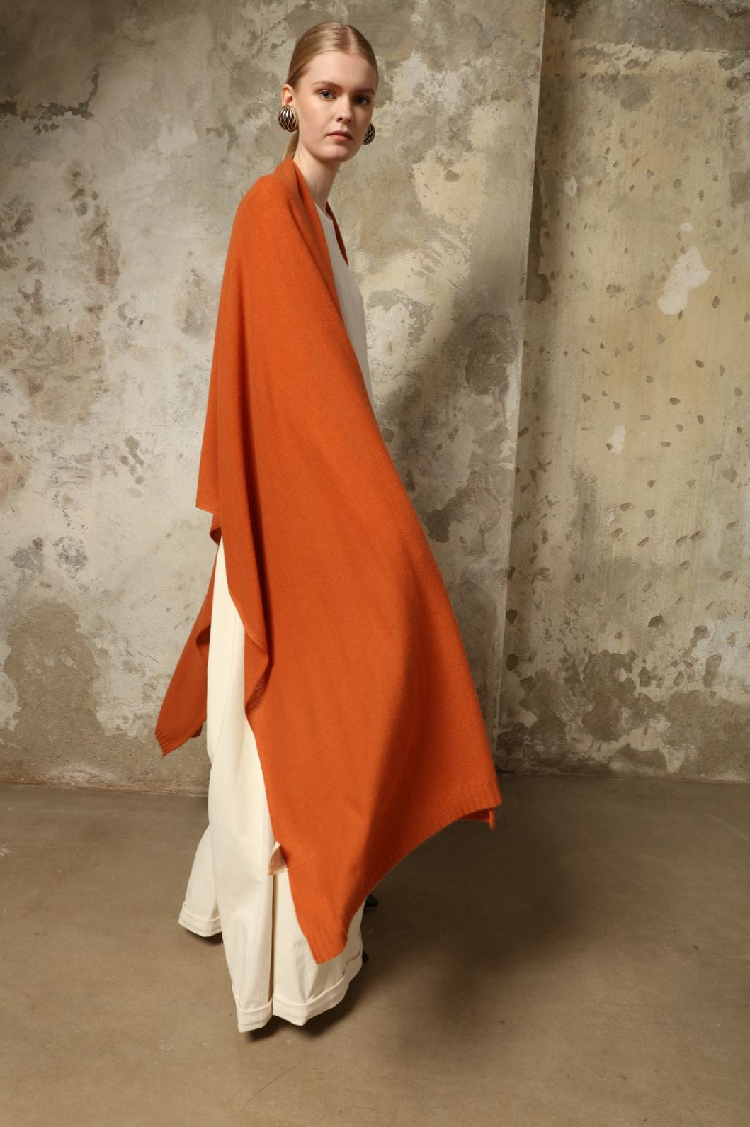 Model is wearing the Brick Leni Scarf by House of Nomad Stories, a pure ethically sourced cashmere scarf with refined texture, enduring softness and fluid drape in a warm brick tone.