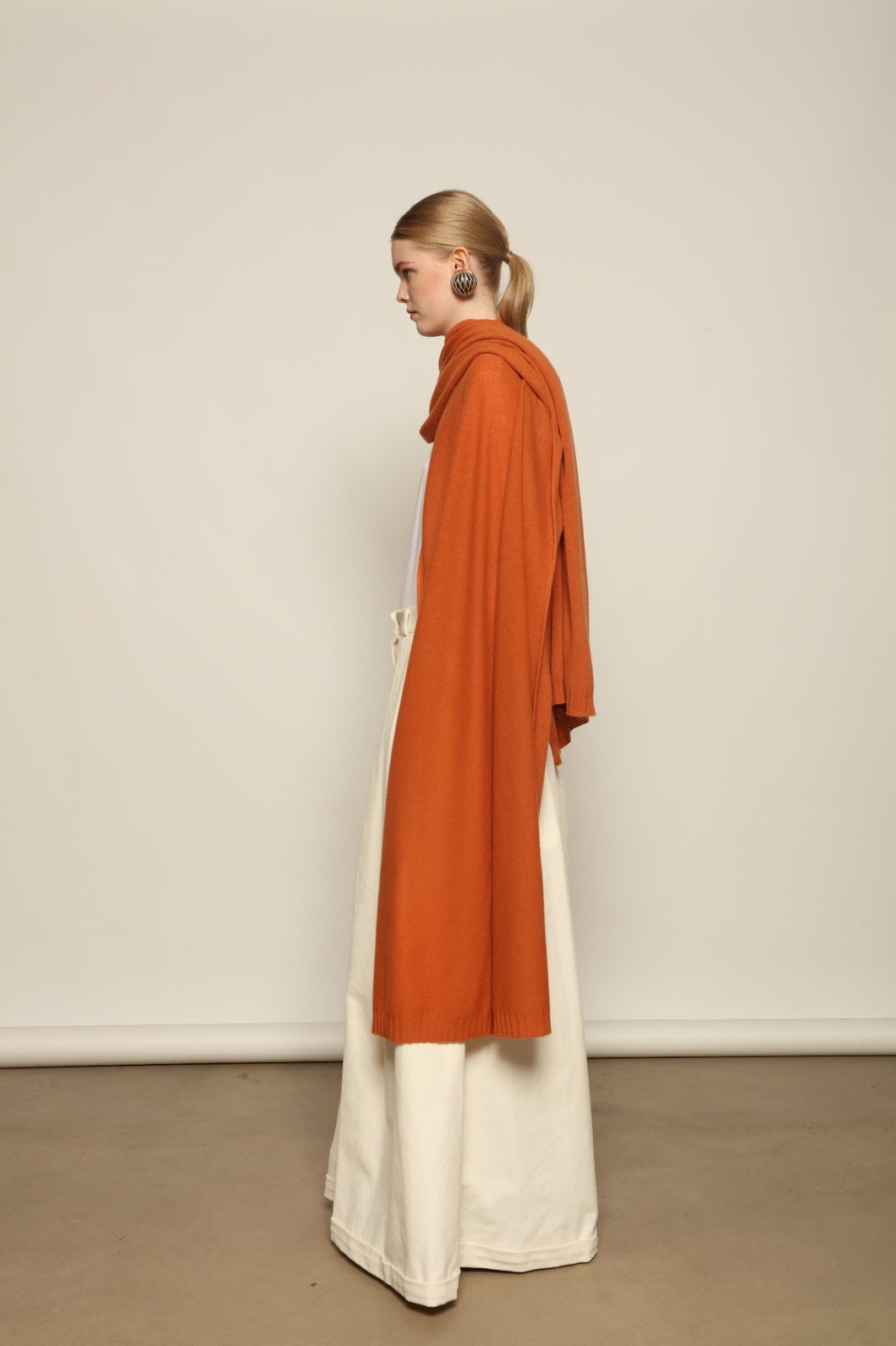Model is wearing the Brick Leni Scarf by House of Nomad Stories, a pure ethically sourced cashmere scarf with refined texture, enduring softness and fluid drape in a warm brick tone.