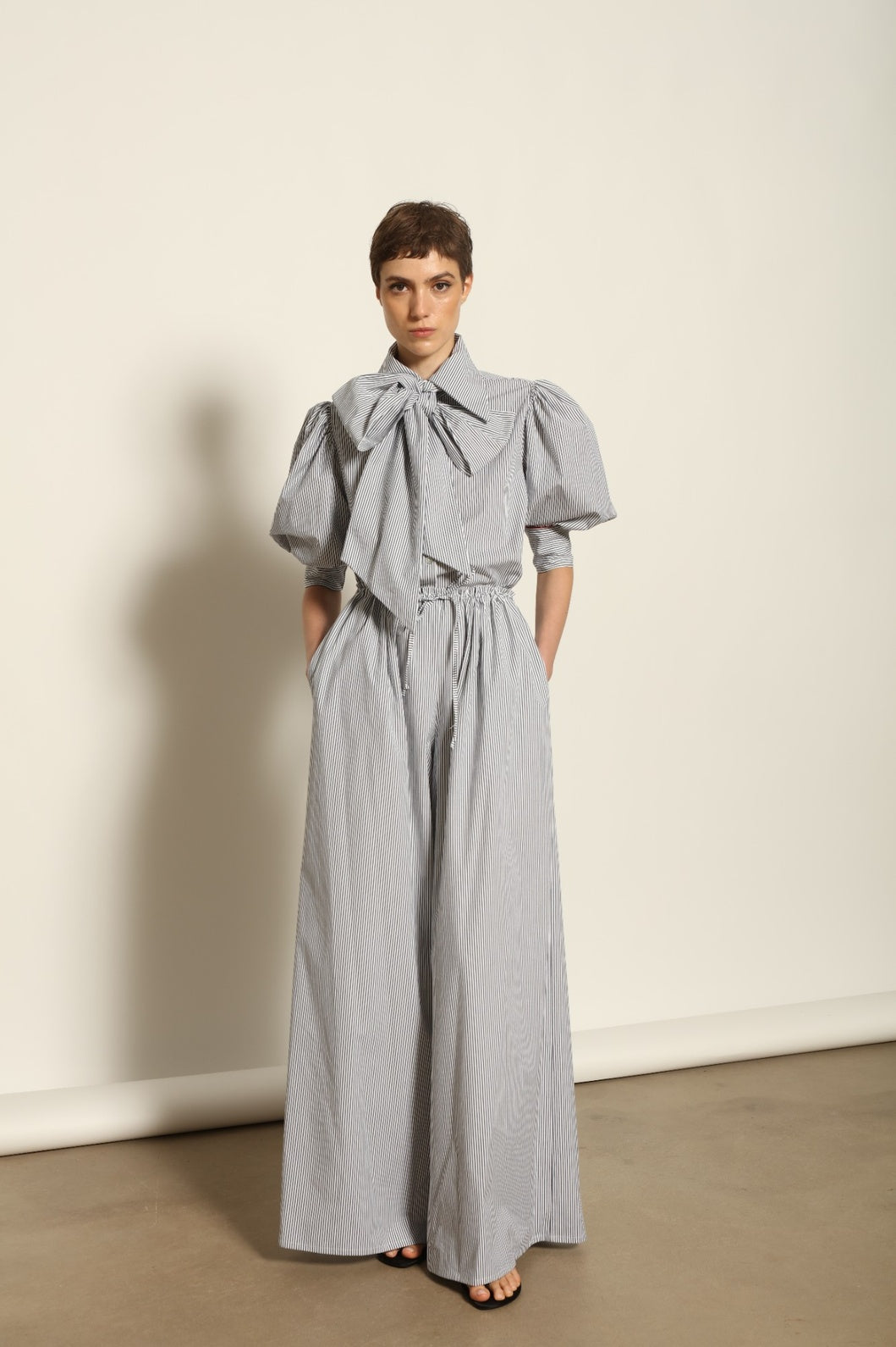 Model wearing the Brigitta White Navy Striped Trousers by House of Nomad Stories, featuring 100% organic cotton fabric, high-rise waist, wide-leg silhouette, and classic white and navy stripes.