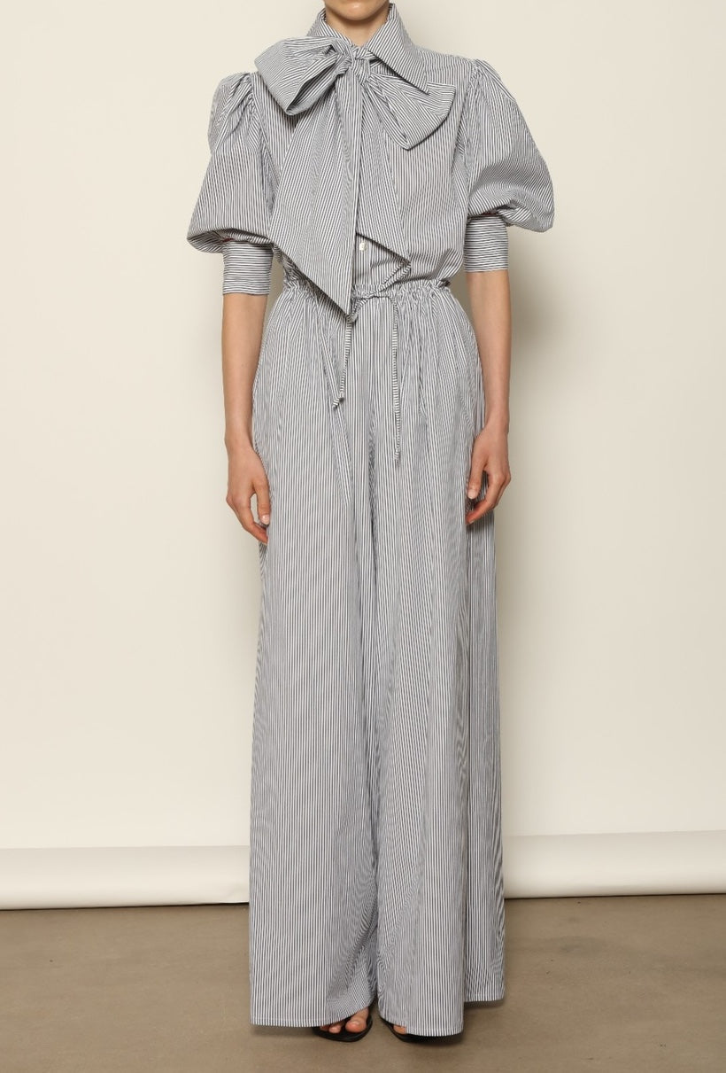Model wearing the Brigitta White Navy Striped Trousers by House of Nomad Stories, featuring 100% organic cotton fabric, high-rise waist, wide-leg silhouette, and classic white and navy stripes.