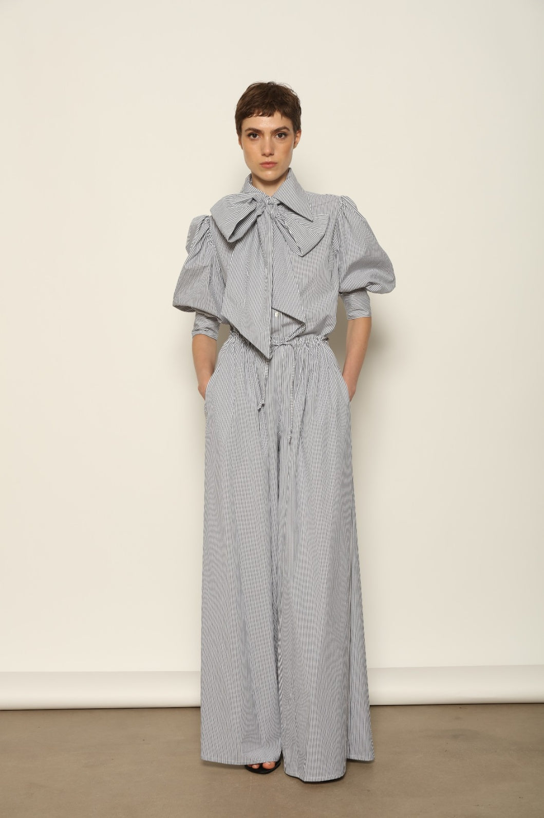 Model wearing the Brigitta White Navy Striped Trousers by House of Nomad Stories, featuring 100% organic cotton fabric, high-rise waist, wide-leg silhouette, and classic white and navy stripes.