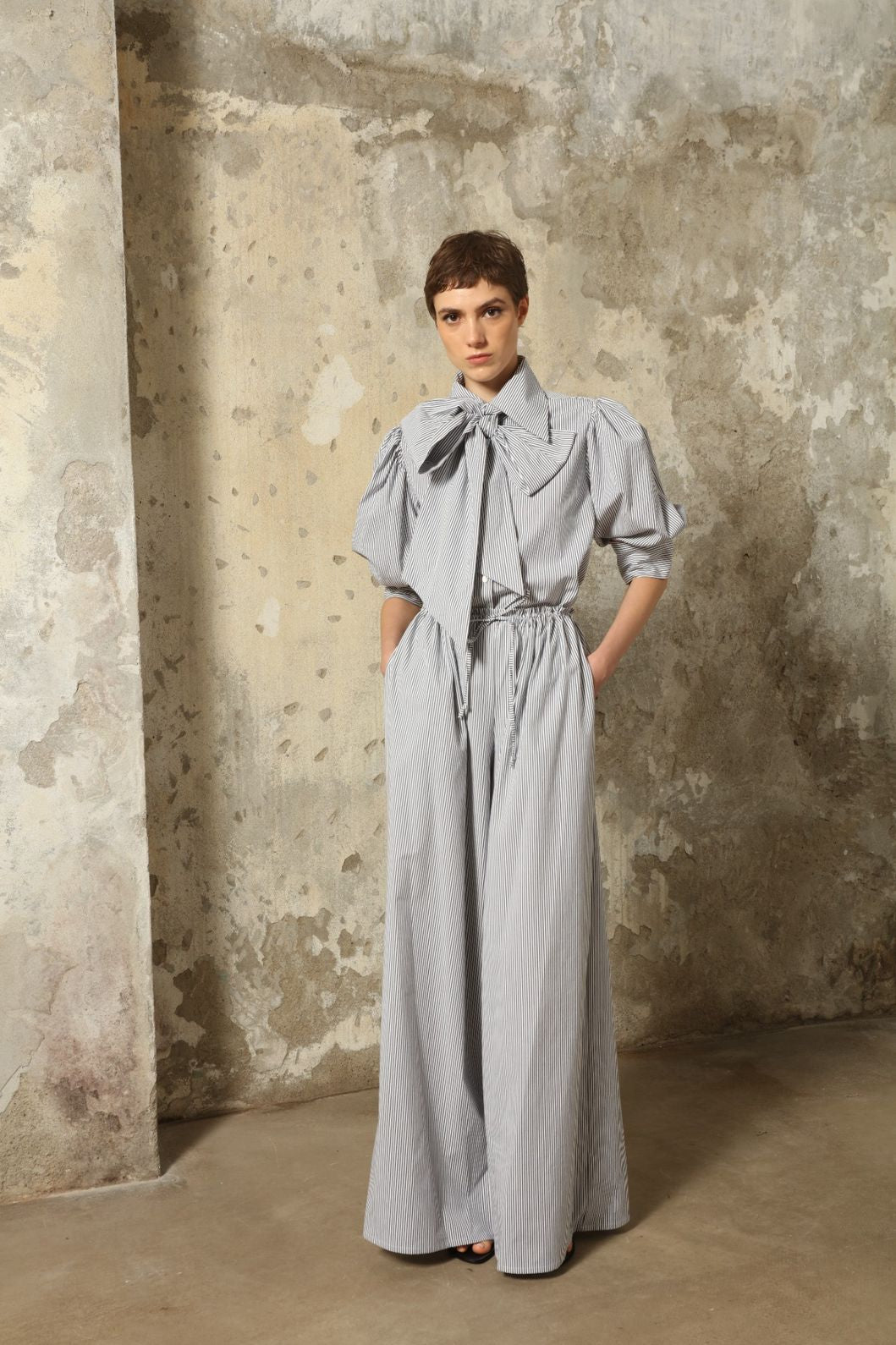 Model wearing the Brigitta White Navy Striped Trousers by House of Nomad Stories, featuring 100% organic cotton fabric, high-rise waist, wide-leg silhouette, and classic white and navy stripes.