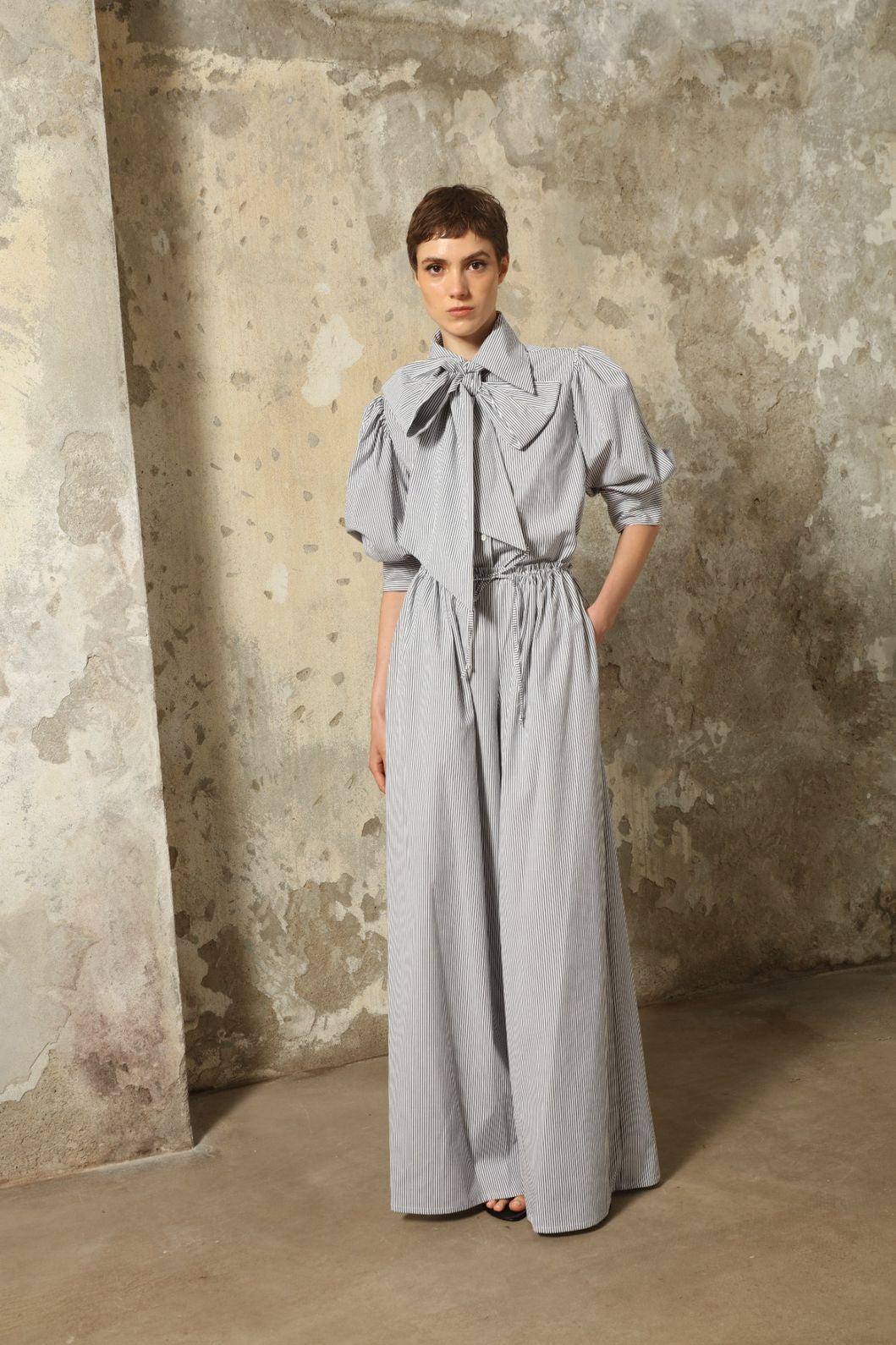 Model wearing the Brigitta White Navy Striped Trousers by House of Nomad Stories, featuring 100% organic cotton fabric, high-rise waist, wide-leg silhouette, and classic white and navy stripes.