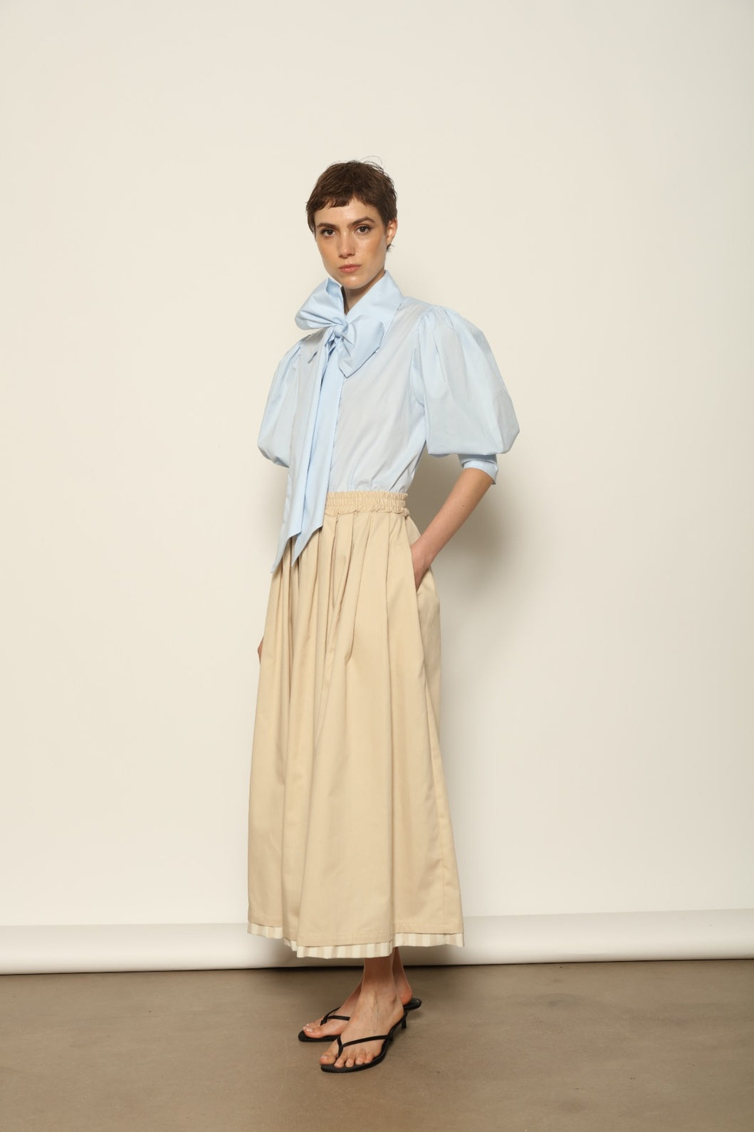 Model wearing the Seoul Camel Skirt by House of Nomad Stories, featuring a structured camel-toned fabric, high-waisted fit, and a clean tailored silhouette with defined architectural lines.