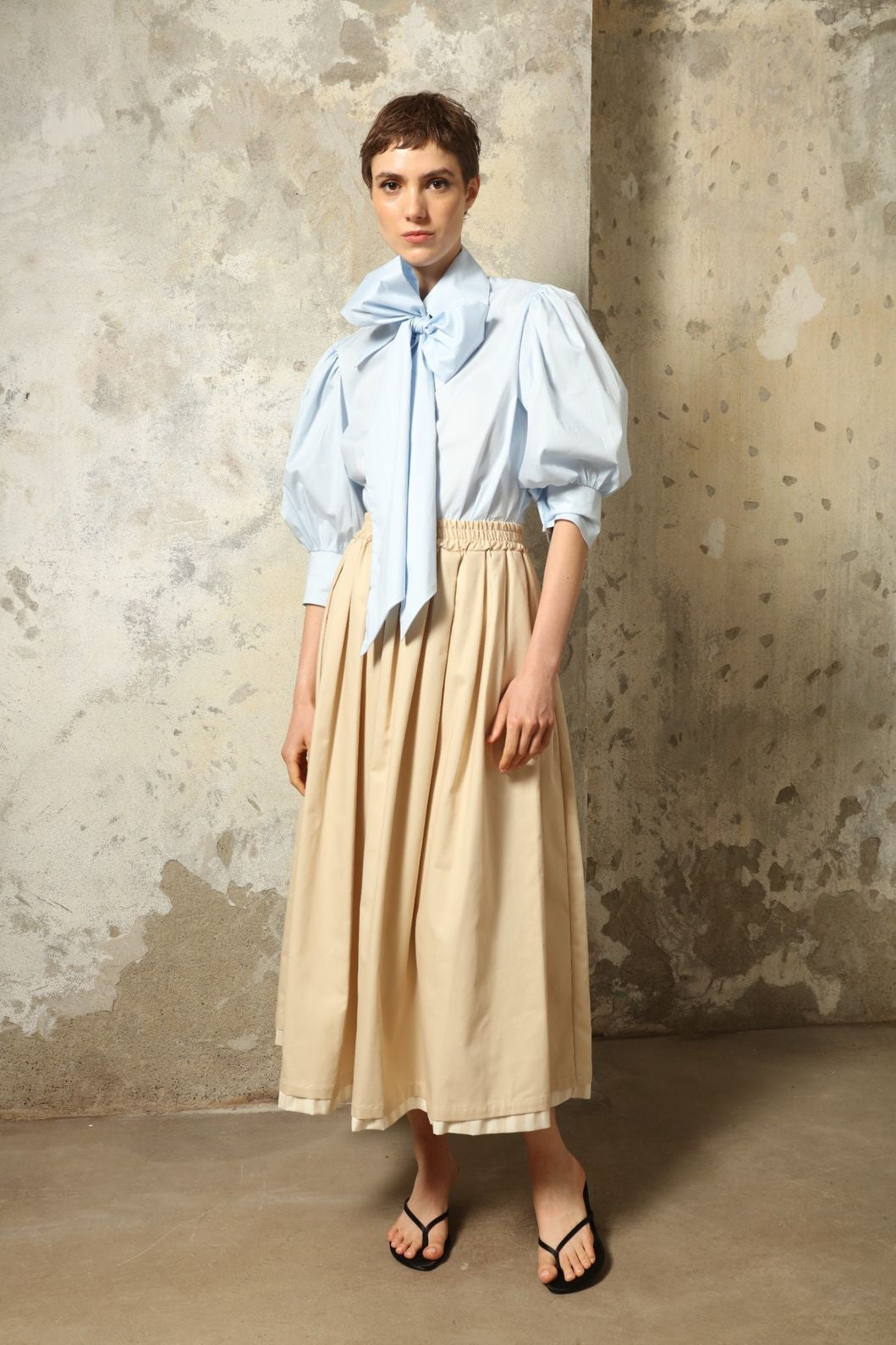 Model wearing the Seoul Camel Skirt by House of Nomad Stories, featuring a structured camel-toned fabric, high-waisted fit, and a clean tailored silhouette with defined architectural lines.