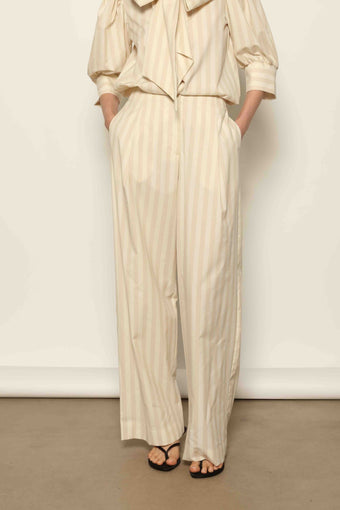 Model wearing the Gabriella Sand White Striped Trousers by House of Nomad Stories, featuring a high-rise waist, straight-leg tailored fit, and soft sand and white stripe pattern in a premium cotton, merino wool, and cashmere blend.