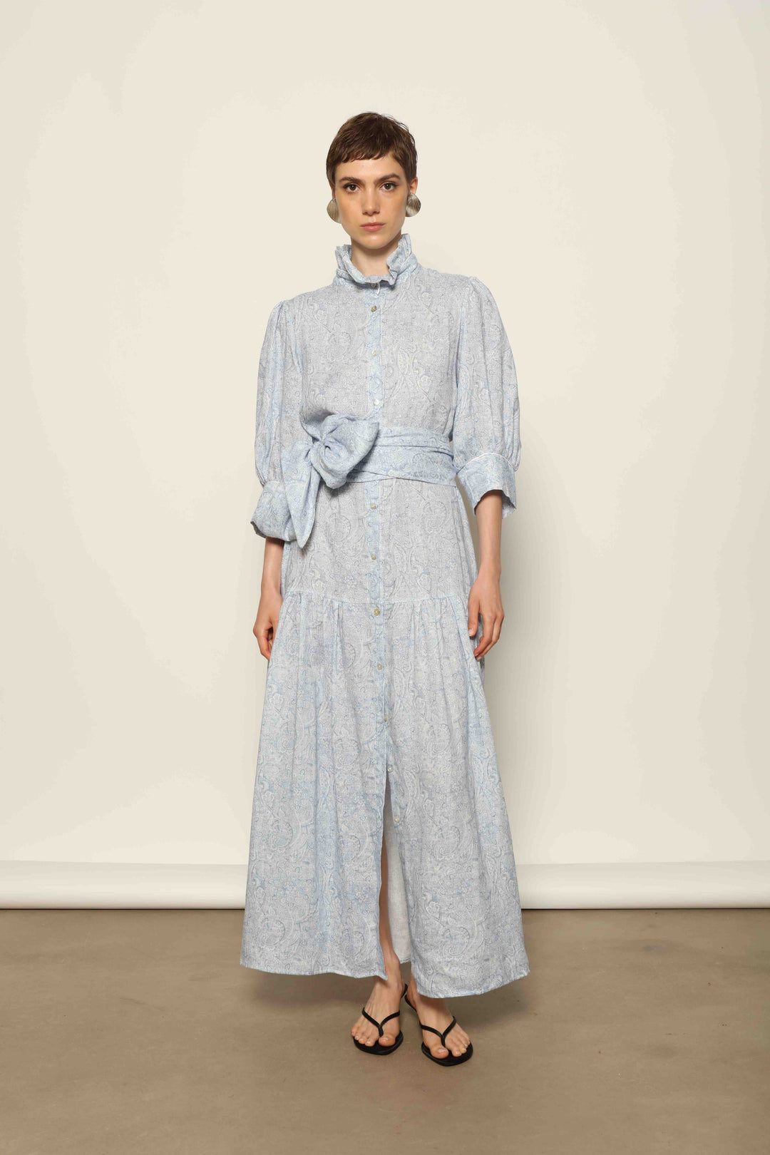 Model wearing the Karin Blue Paisley Dress by House of Nomad Stories, featuring 100% linen fabric, soft blue paisley print, and a relaxed flowing silhouette with breathable lightweight structure.