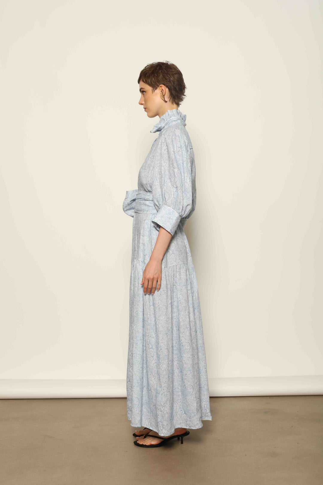 Model wearing the Karin Blue Paisley Dress by House of Nomad Stories, featuring 100% linen fabric, soft blue paisley print, and a relaxed flowing silhouette with breathable lightweight structure.
