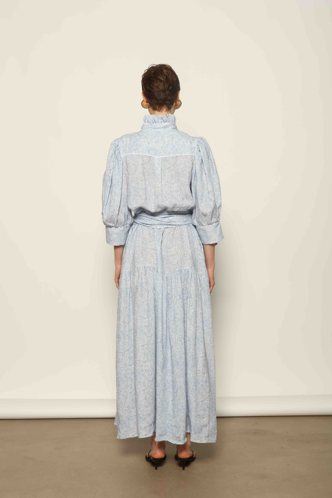 Model wearing the Karin Blue Paisley Dress by House of Nomad Stories, featuring 100% linen fabric, soft blue paisley print, and a relaxed flowing silhouette with breathable lightweight structure.