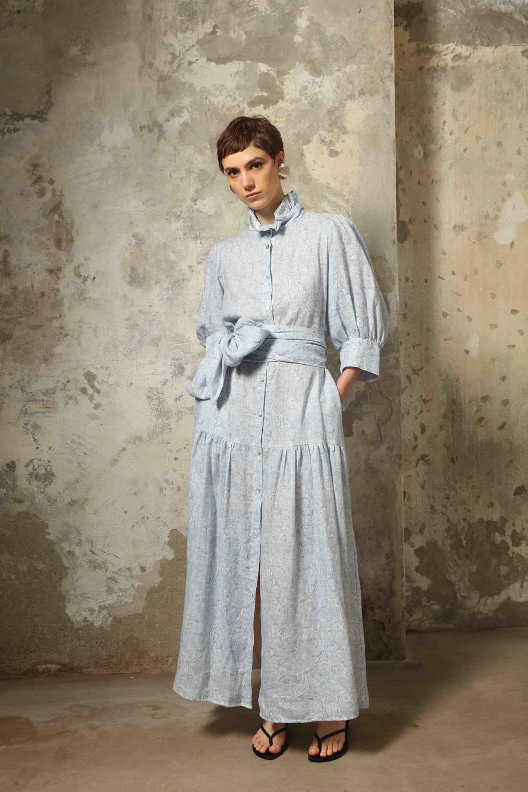 Model wearing the Karin Blue Paisley Dress by House of Nomad Stories, featuring 100% linen fabric, soft blue paisley print, and a relaxed flowing silhouette with breathable lightweight structure.