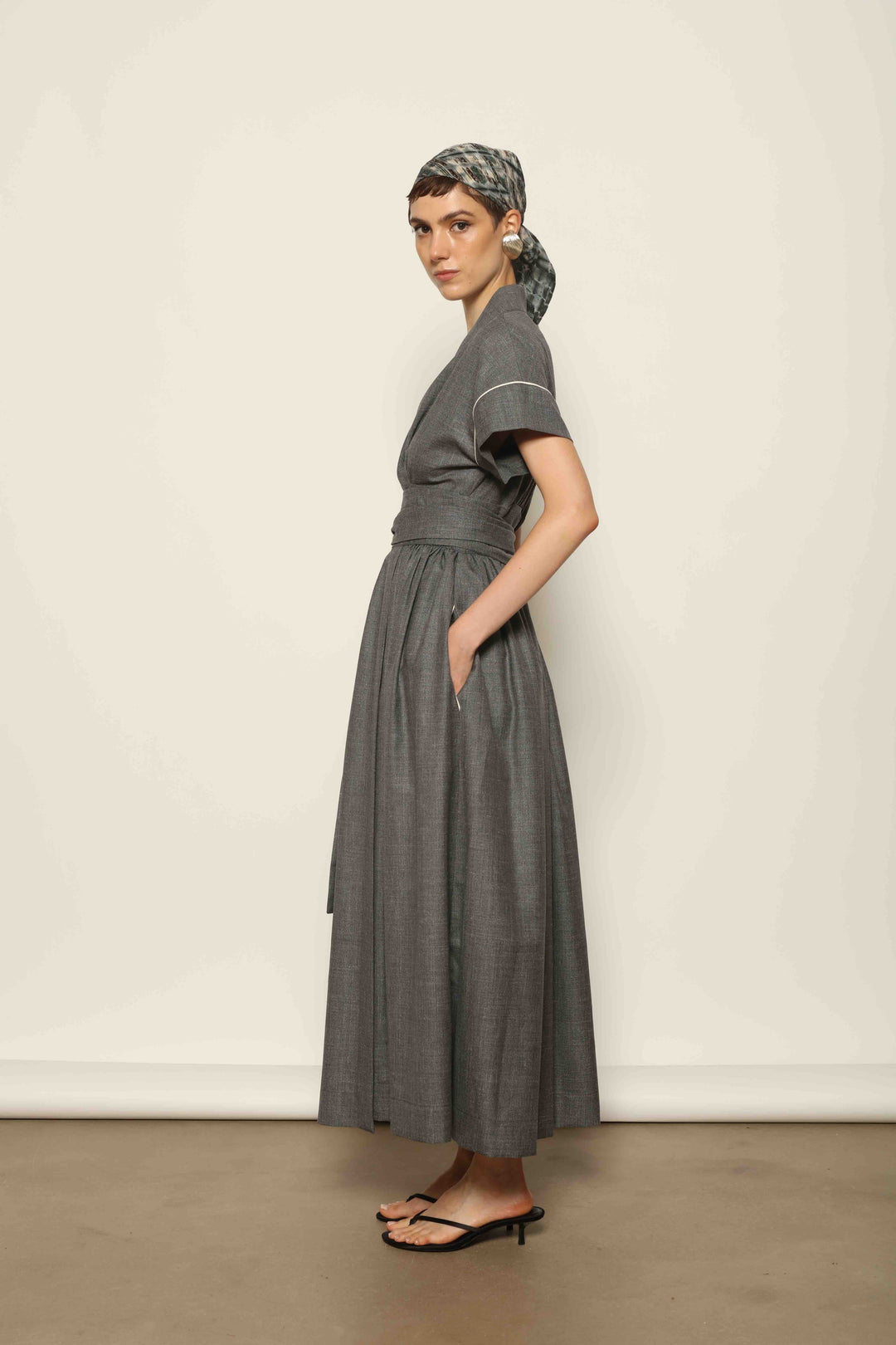 Model wearing the Saint Remy Grey Off White Midi Dress by House of Nomad Stories, featuring a wrap silhouette, adjustable belt, half sleeves, and subtle white piping detail in a fluid elegant fabric.