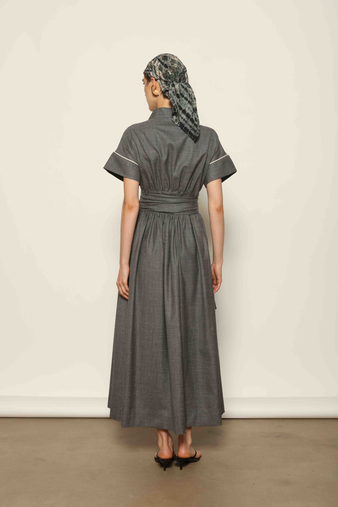 Model wearing the Saint Remy Grey Off White Midi Dress by House of Nomad Stories, featuring a wrap silhouette, adjustable belt, half sleeves, and subtle white piping detail in a fluid elegant fabric.