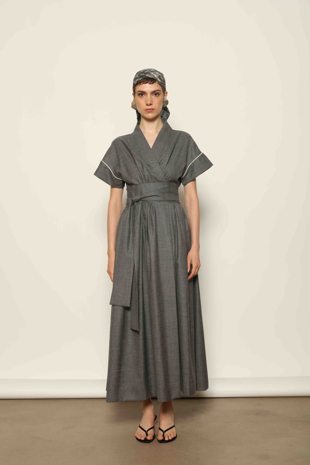 Model wearing the Saint Remy Grey Off White Midi Dress by House of Nomad Stories, featuring a wrap silhouette, adjustable belt, half sleeves, and subtle white piping detail in a fluid elegant fabric.