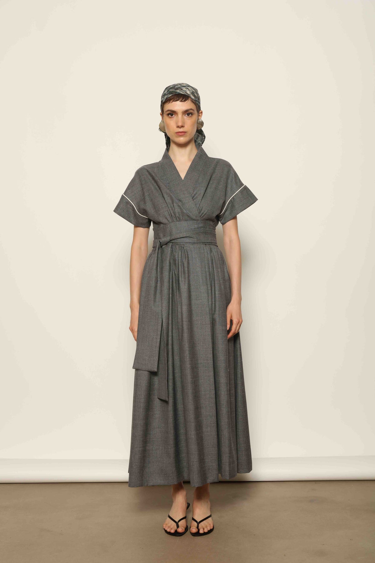 Model wearing the Saint Remy Grey Off White Midi Dress by House of Nomad Stories, featuring a wrap silhouette, adjustable belt, half sleeves, and subtle white piping detail in a fluid elegant fabric.