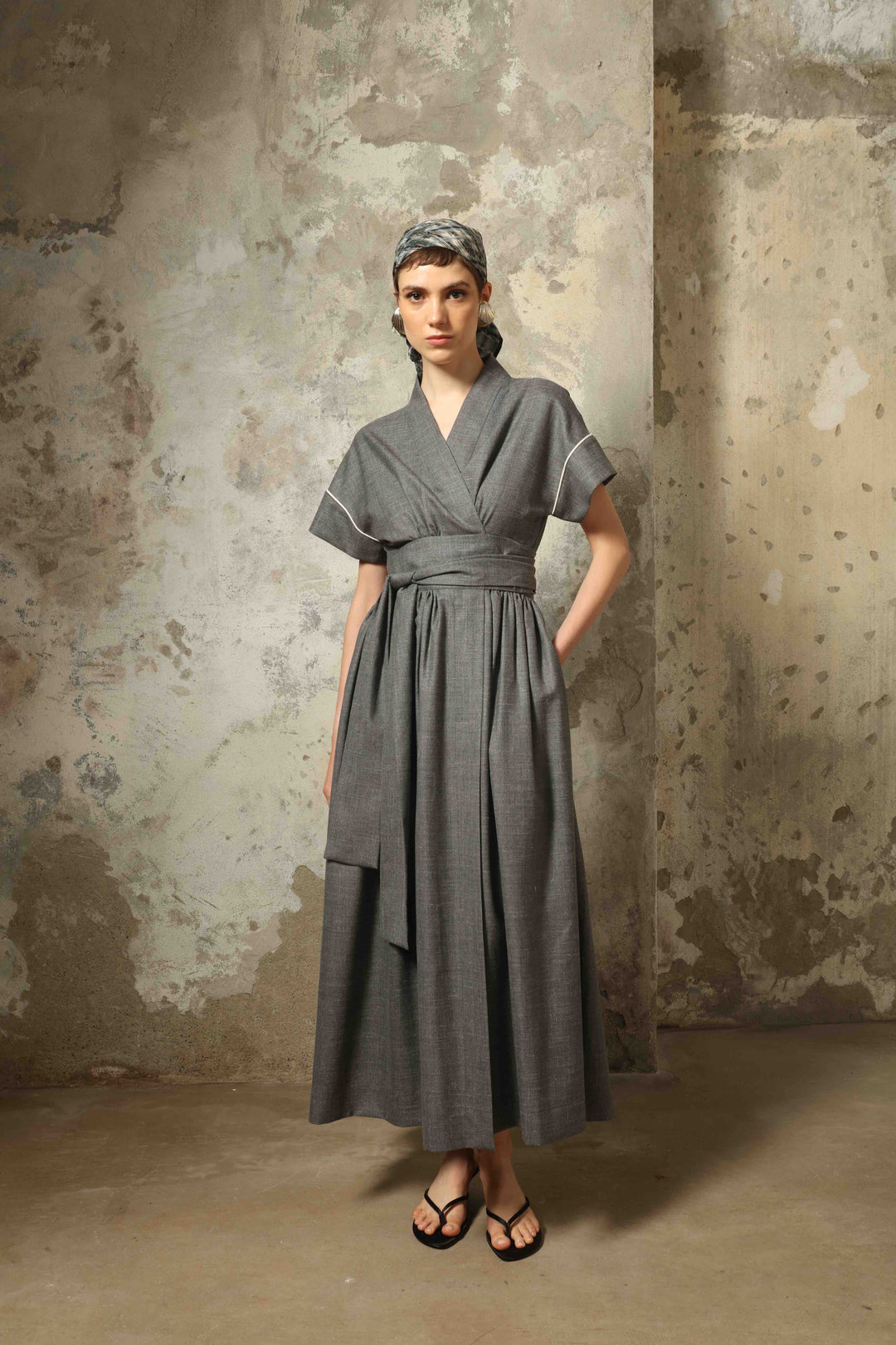 Model wearing the Saint Remy Grey Off White Midi Dress by House of Nomad Stories, featuring a wrap silhouette, adjustable belt, half sleeves, and subtle white piping detail in a fluid elegant fabric.
