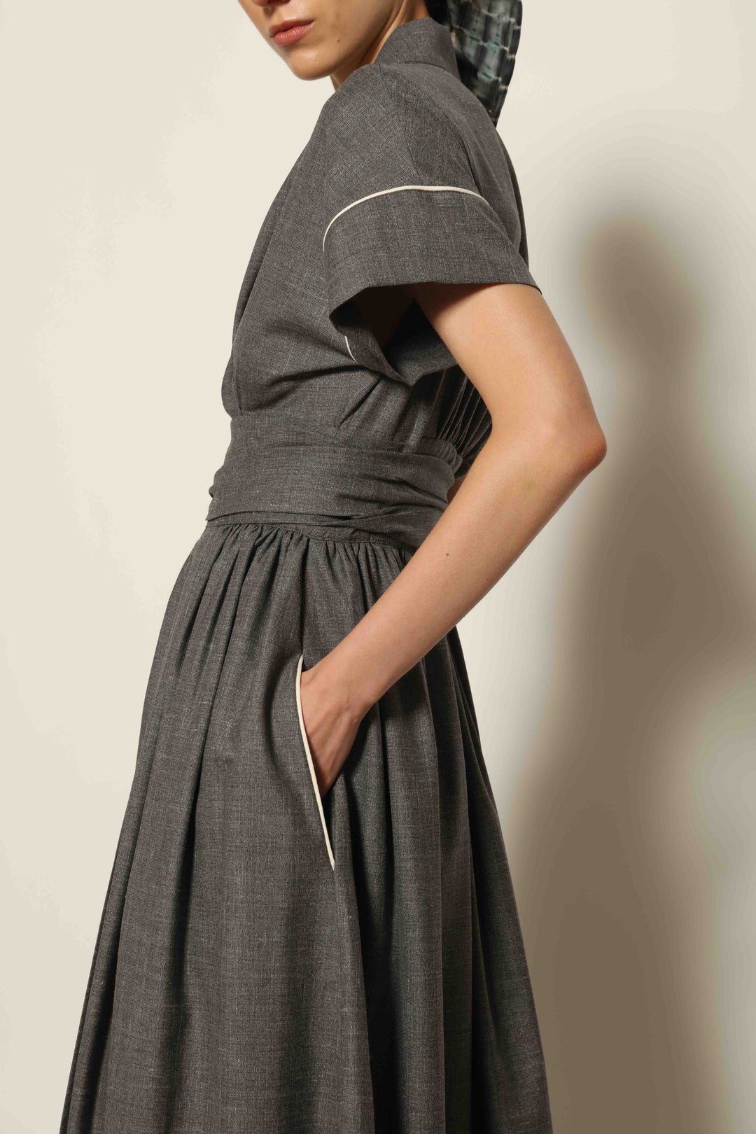 Model wearing the Saint Remy Grey Off White Midi Dress by House of Nomad Stories, featuring a wrap silhouette, adjustable belt, half sleeves, and subtle white piping detail in a fluid elegant fabric.