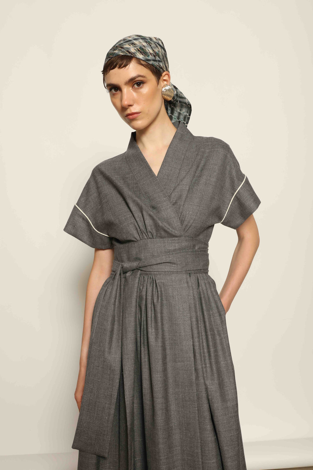 Model wearing the Saint Remy Grey Off White Midi Dress by House of Nomad Stories, featuring a wrap silhouette, adjustable belt, half sleeves, and subtle white piping detail in a fluid elegant fabric.