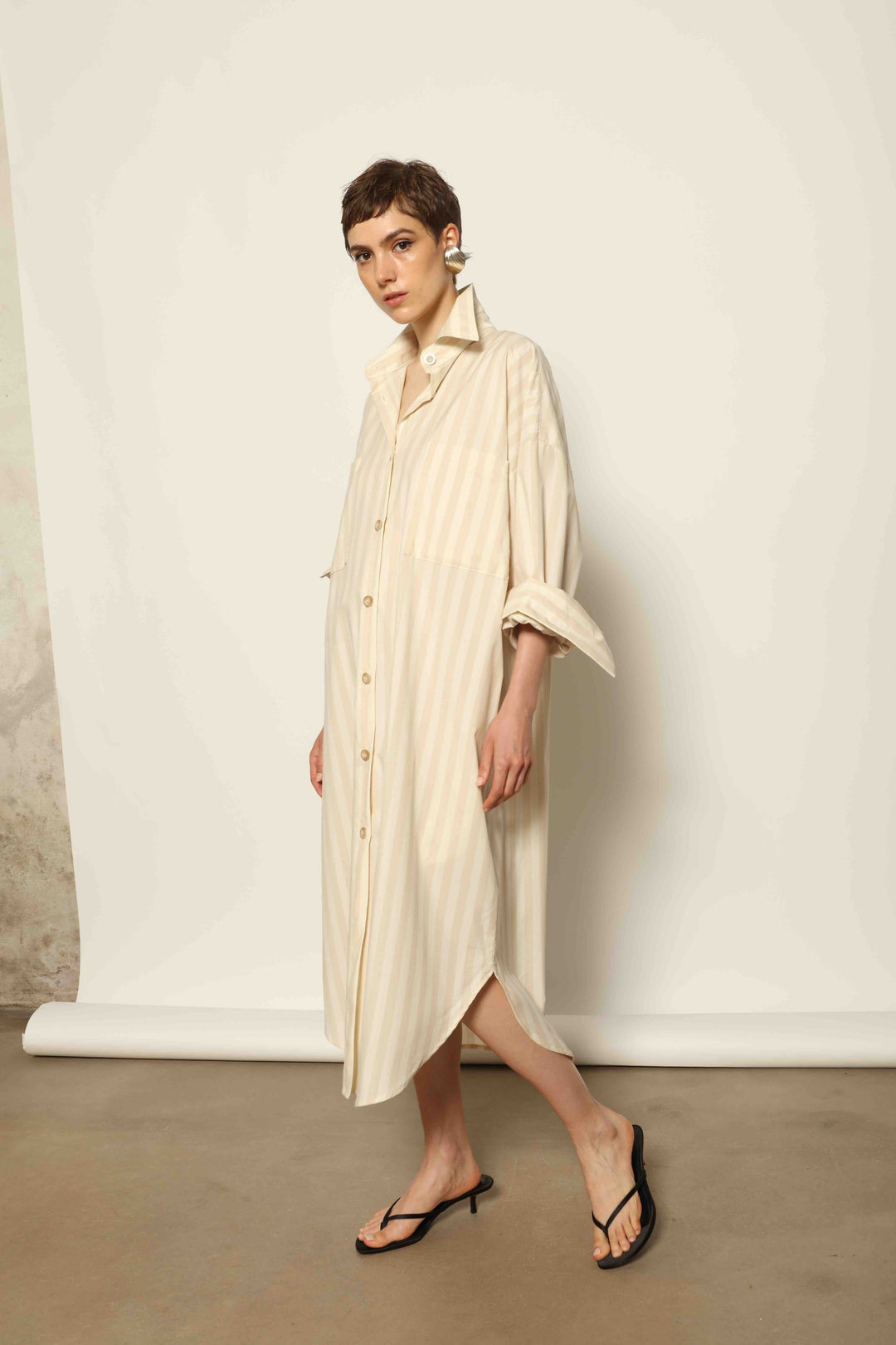 Model is wearing the Sand White Striped Bettina Dress by House of Nomad Stories, featuring a fluid silhouette with subtle sand and white vertical stripes and a soft, elegant drape.