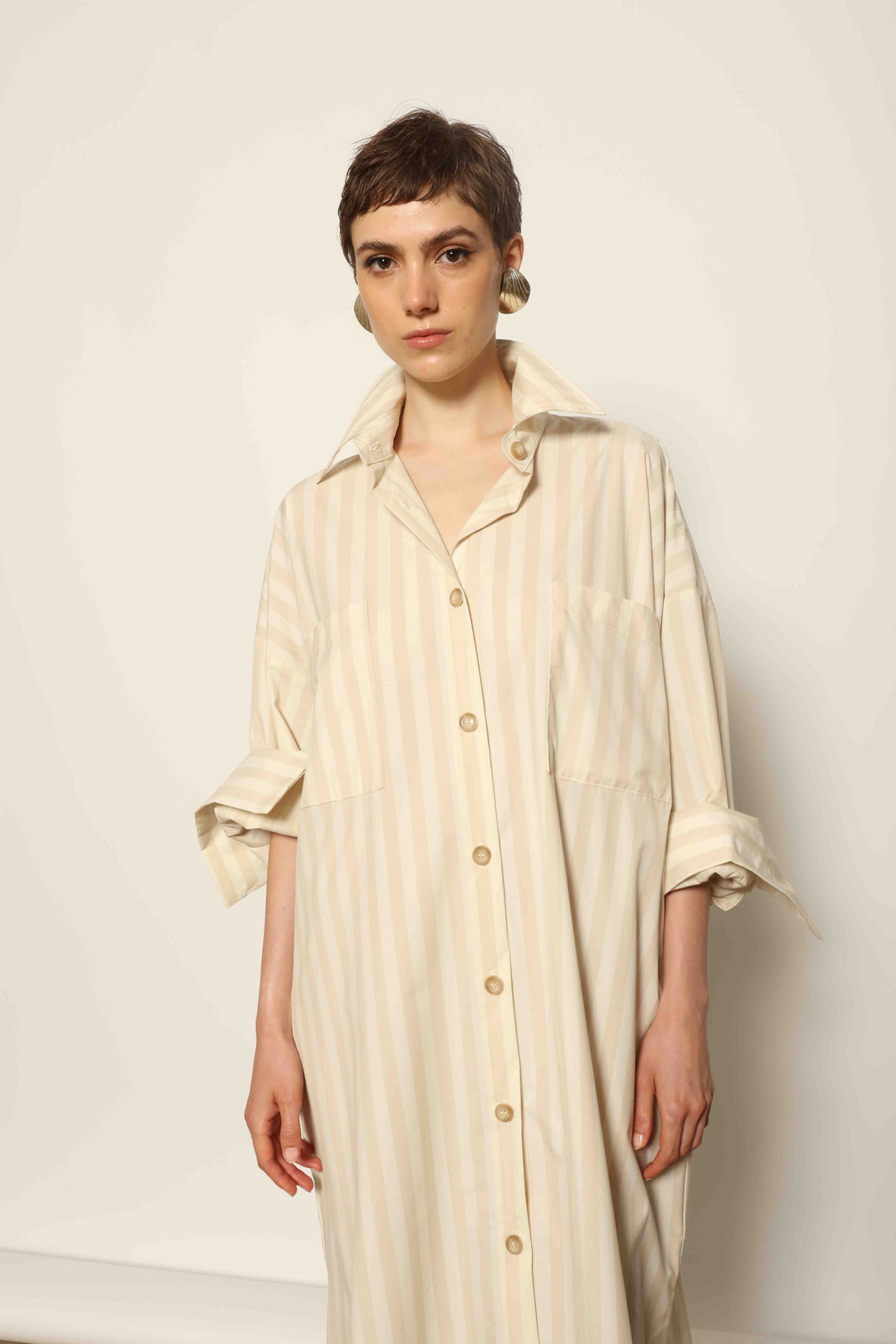Model is wearing the Sand White Striped Bettina Dress by House of Nomad Stories, featuring a fluid silhouette with subtle sand and white vertical stripes and a soft, elegant drape.