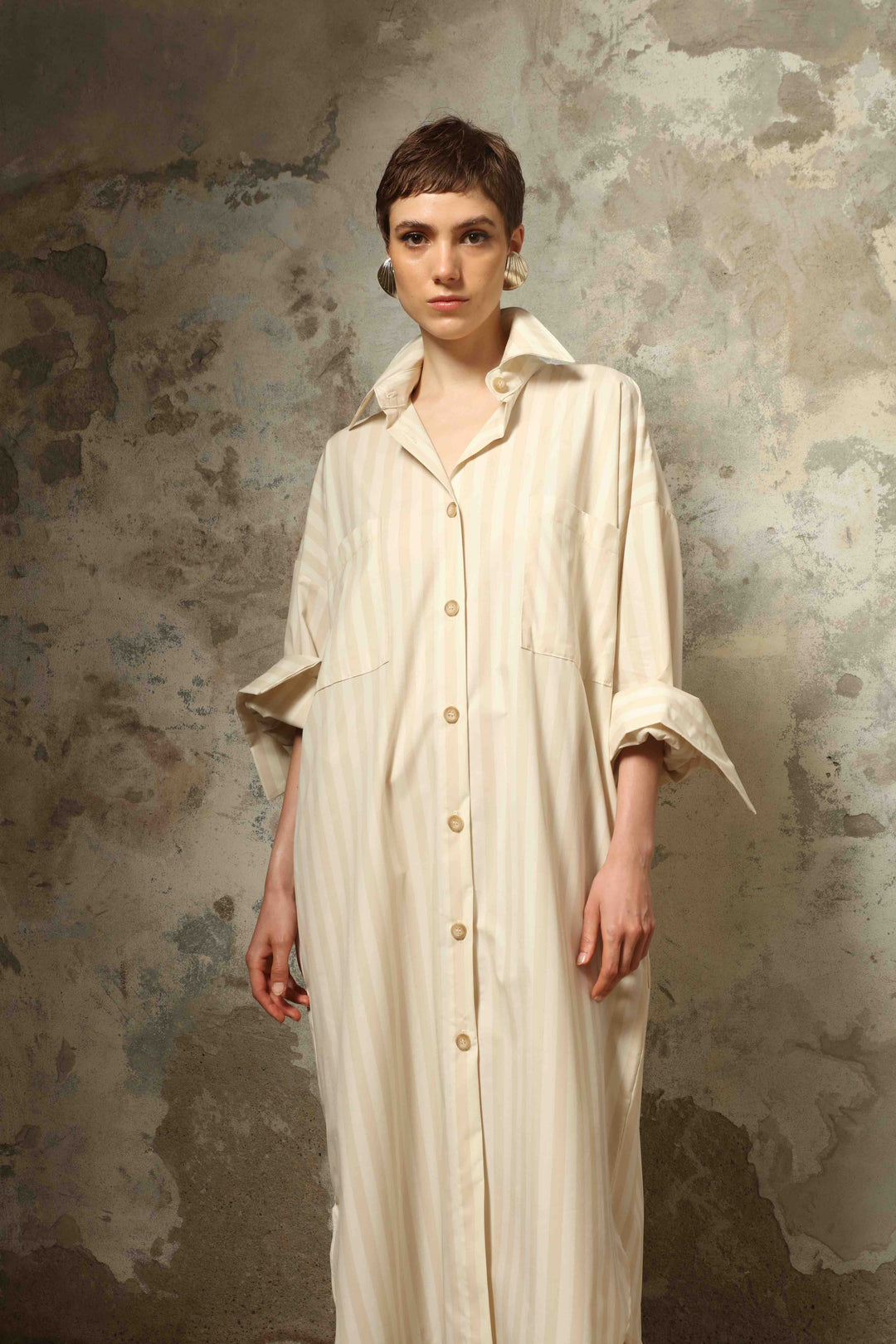 Model is wearing the Sand White Striped Bettina Dress by House of Nomad Stories, featuring a fluid silhouette with subtle sand and white vertical stripes and a soft, elegant drape.